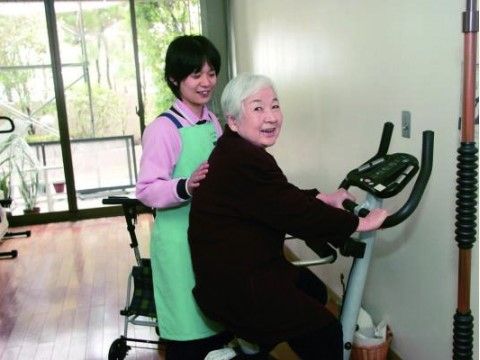 足のリハビリに励む女性住居者様と、サポートをする女性スタッフ