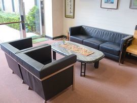 黒いソファーとセンターテーブルが置いてある。手前のソファーは1人がけが2脚並んでいる。壁には書道や絵の入った額縁が掛かっている。
