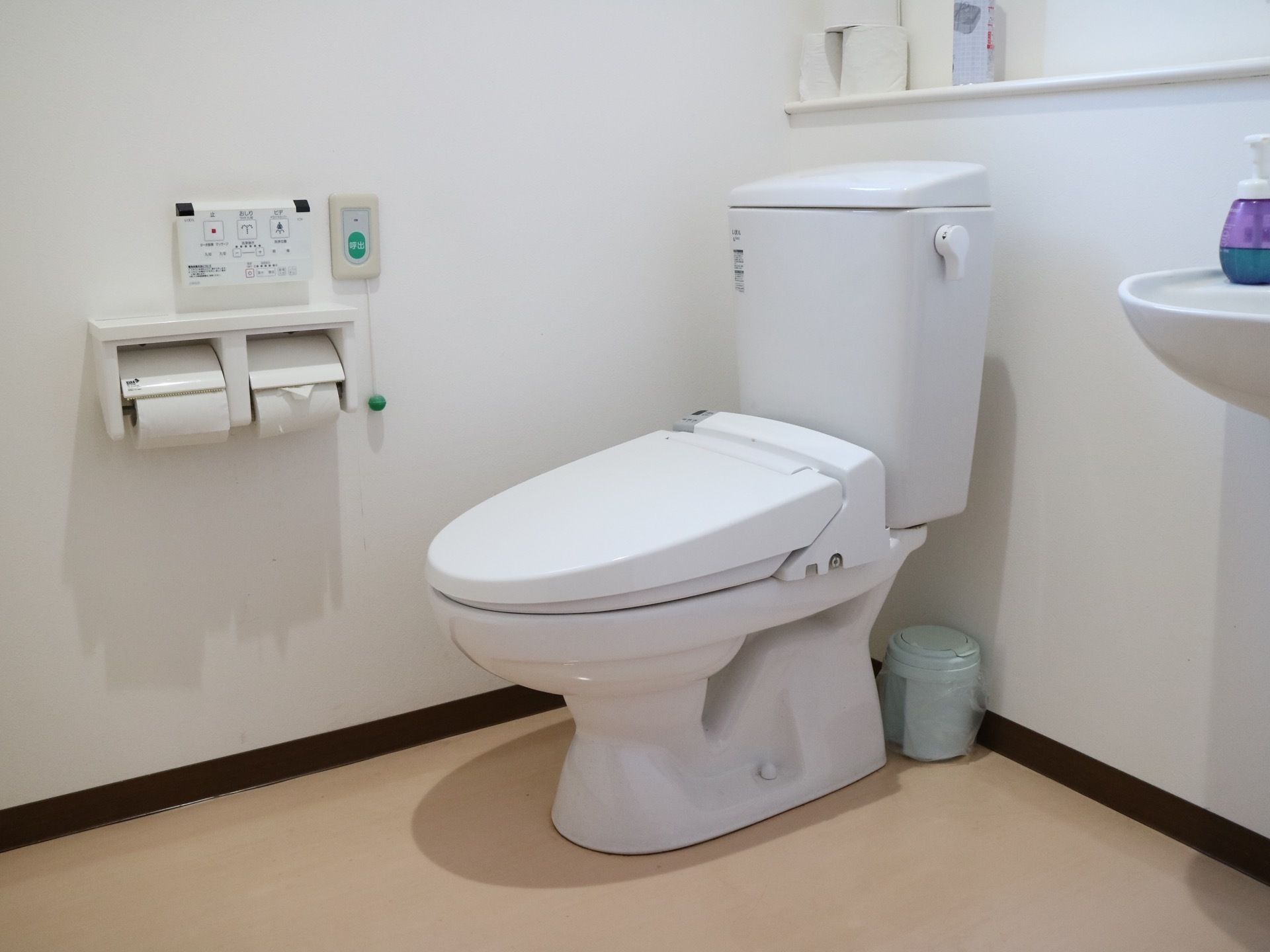 蓋やタンクが付いている洋式便器が据えてある。壁面にトイレットペーパーホルダーや操作ボタンが設置されている。