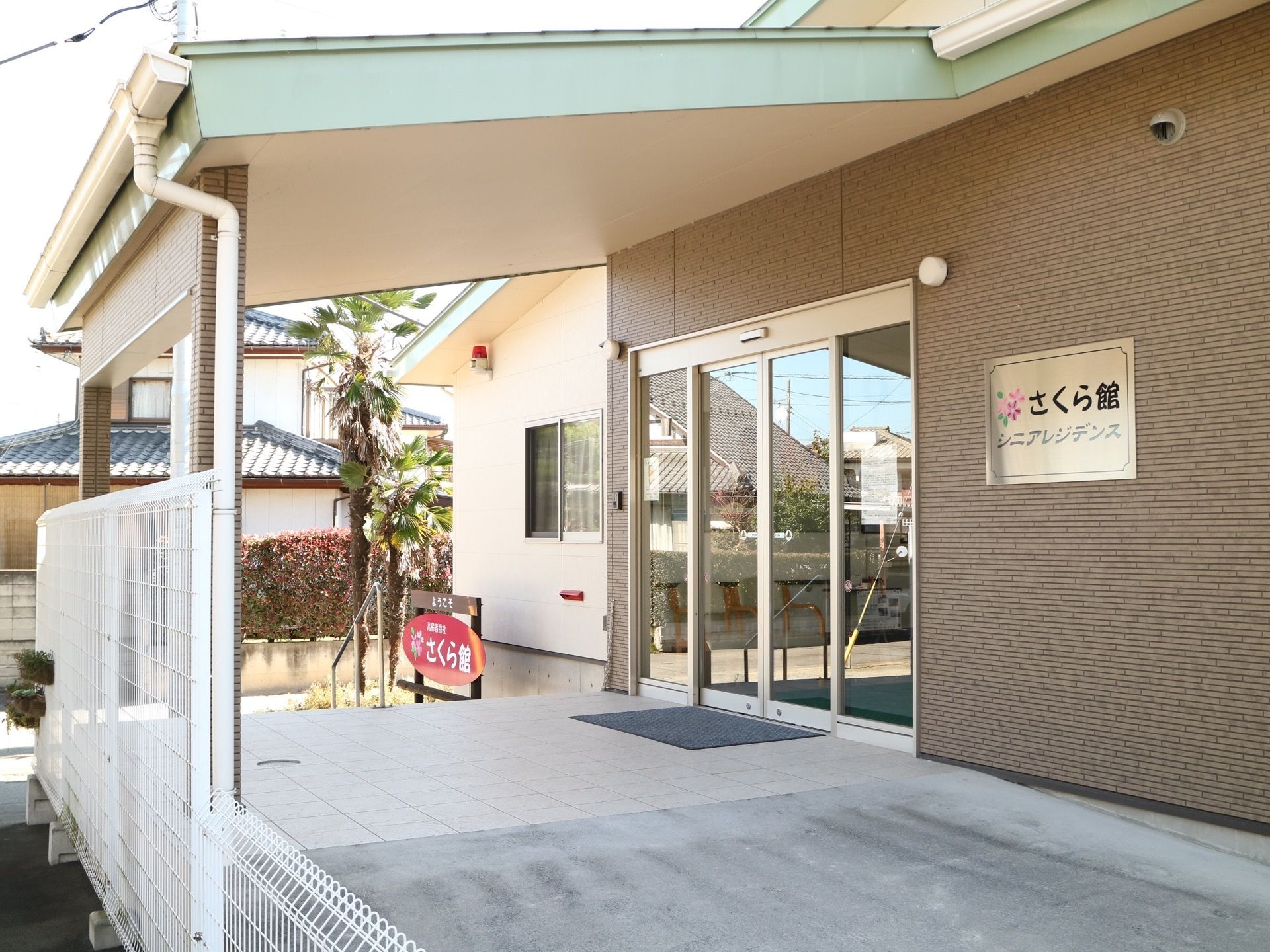 玄関の外側に大きな屋根が張り出している。自動ドアの前方はタイル調に舗装されており、右側にコンクリート製の斜面がある。
