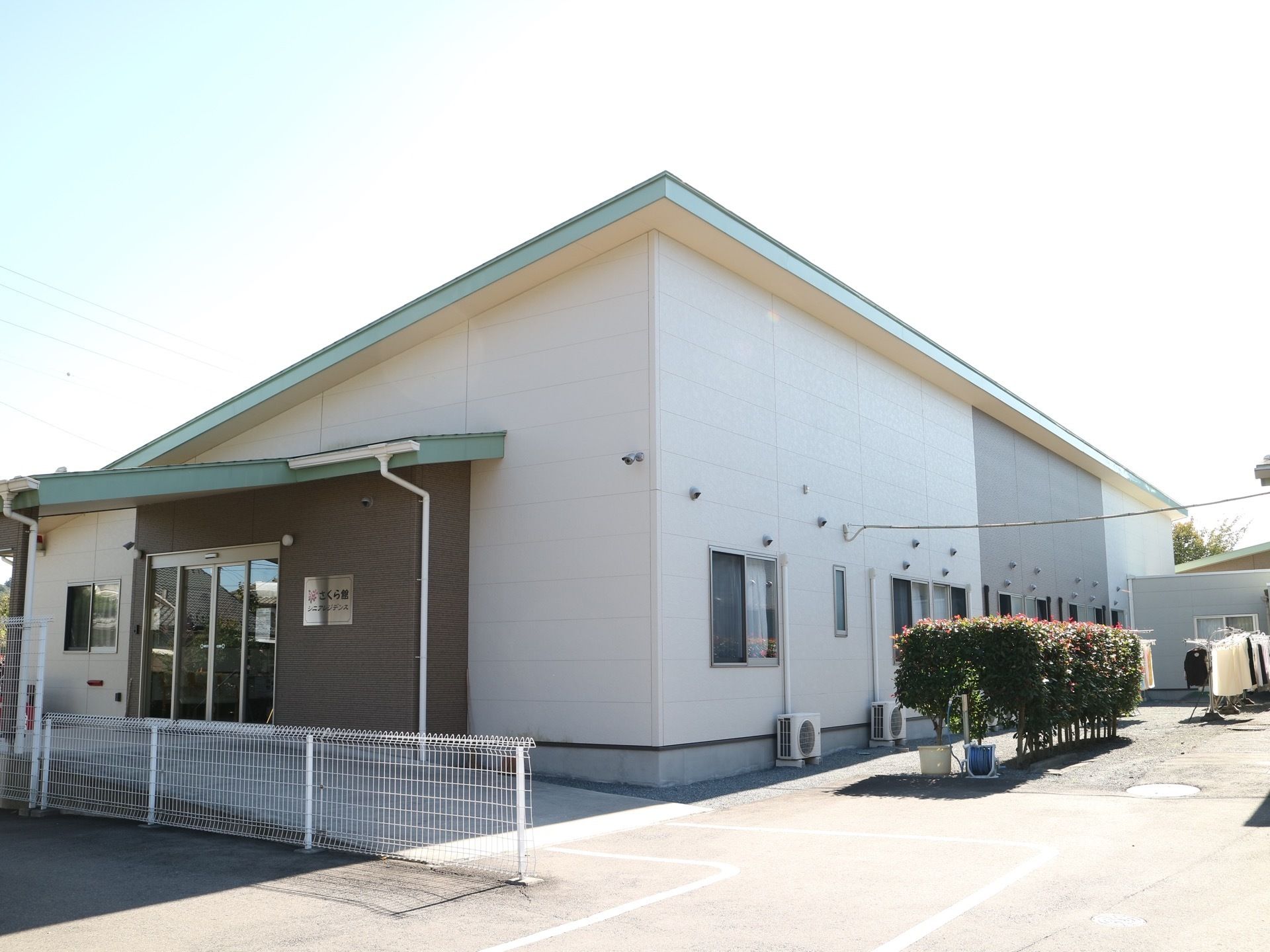舗装された敷地に建っている片流れ屋根の施設である。右側のスペースに物干し台があり、洗濯物が干されている。