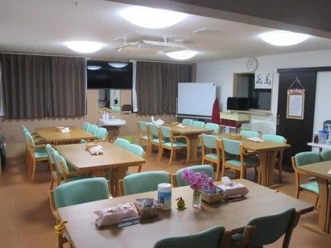 ６人掛けおよび４人掛けテーブルが規則正しく複数台ならんでいる共用スペースである。コーナーにホワイトボードが置かれている。