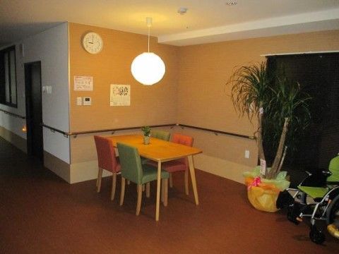通路から続くフロアの一角に、テーブルと椅子が並べられている。観葉植物が置かれ、壁面には手すりが設置されている。