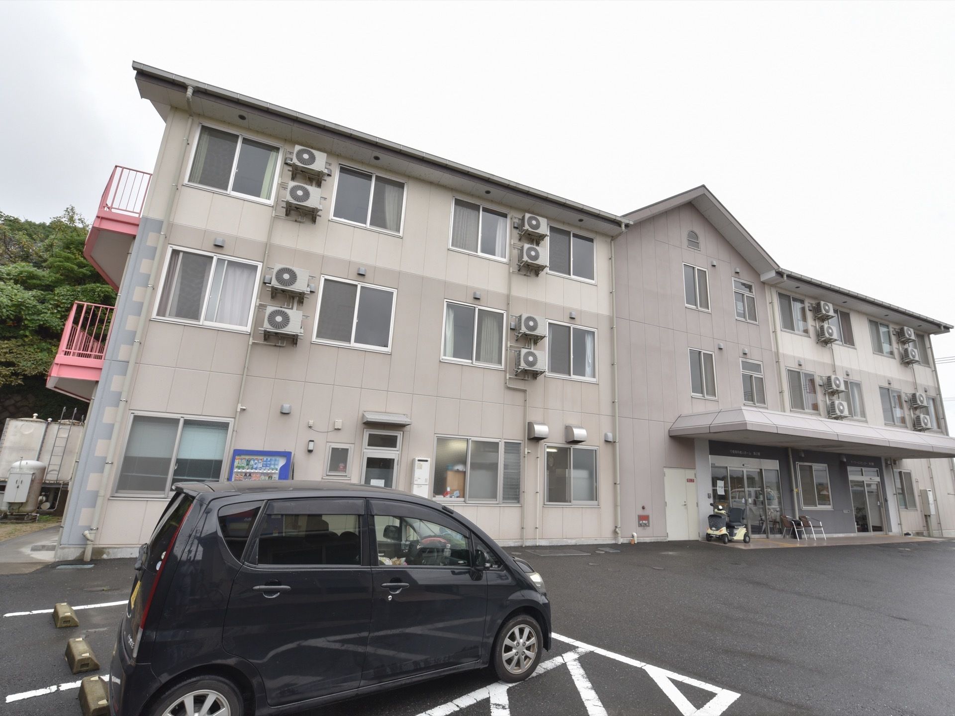 グレーの外壁が落ち着いた雰囲気の３階建ての施設の外観。入り口までのアプローチは段差のないバリアフリーになっている。