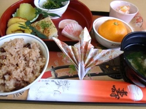 寿と書かれた祝い箸がセットされ、お赤飯とおせち料理が並ぶ豪華な食事