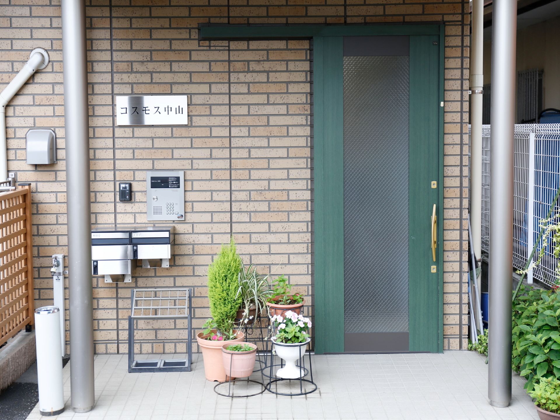 施設の玄関ドアは深いグリーンの引き戸で、中央部分には、すりガラスがはめ込まれている。左側にインターホンがある。