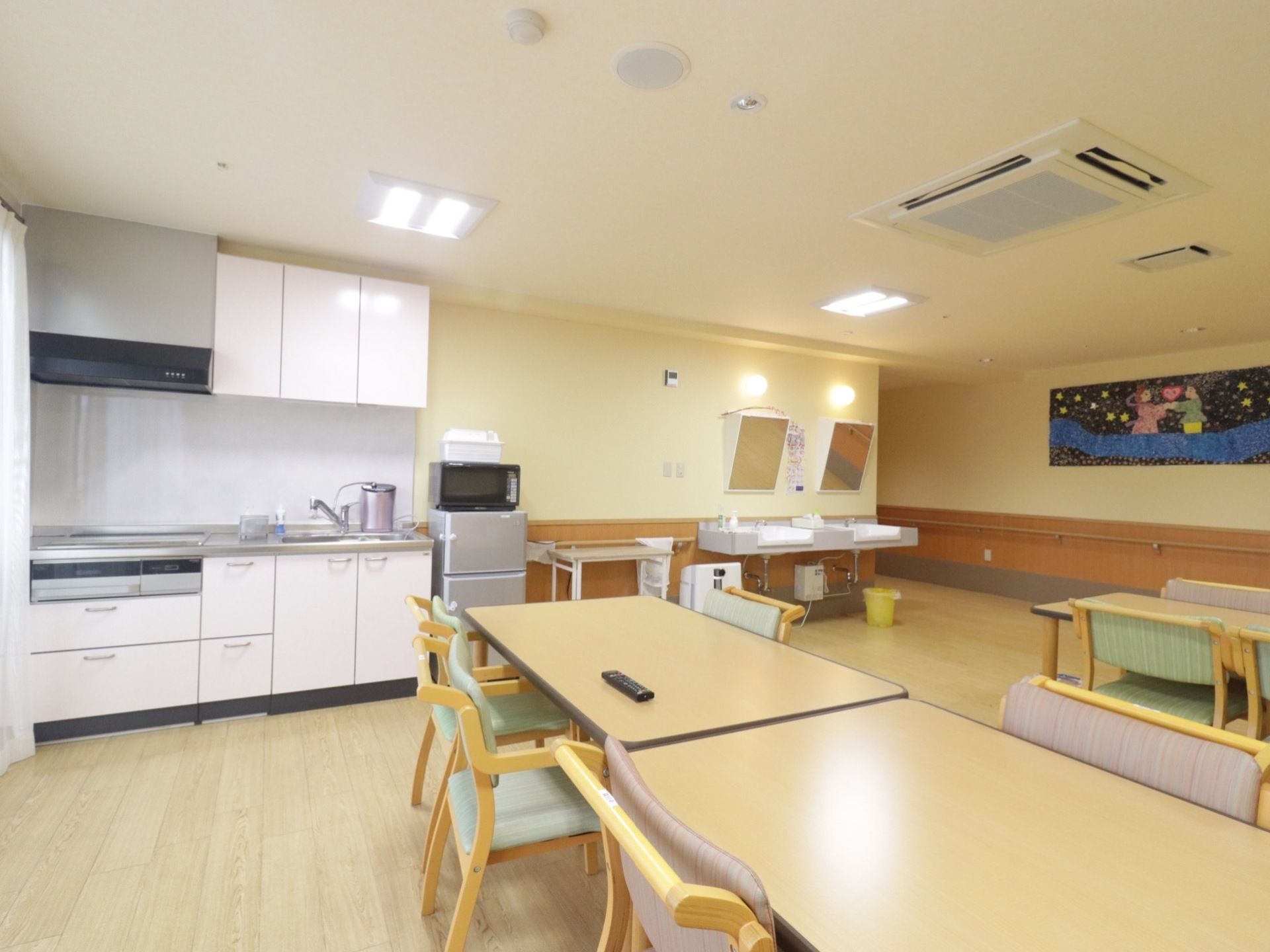 ３～４人掛けの机がいくつかある。奥にはキッチンと冷蔵庫と電子レンジがある。その隣には鏡付きの洗面台が２つある。