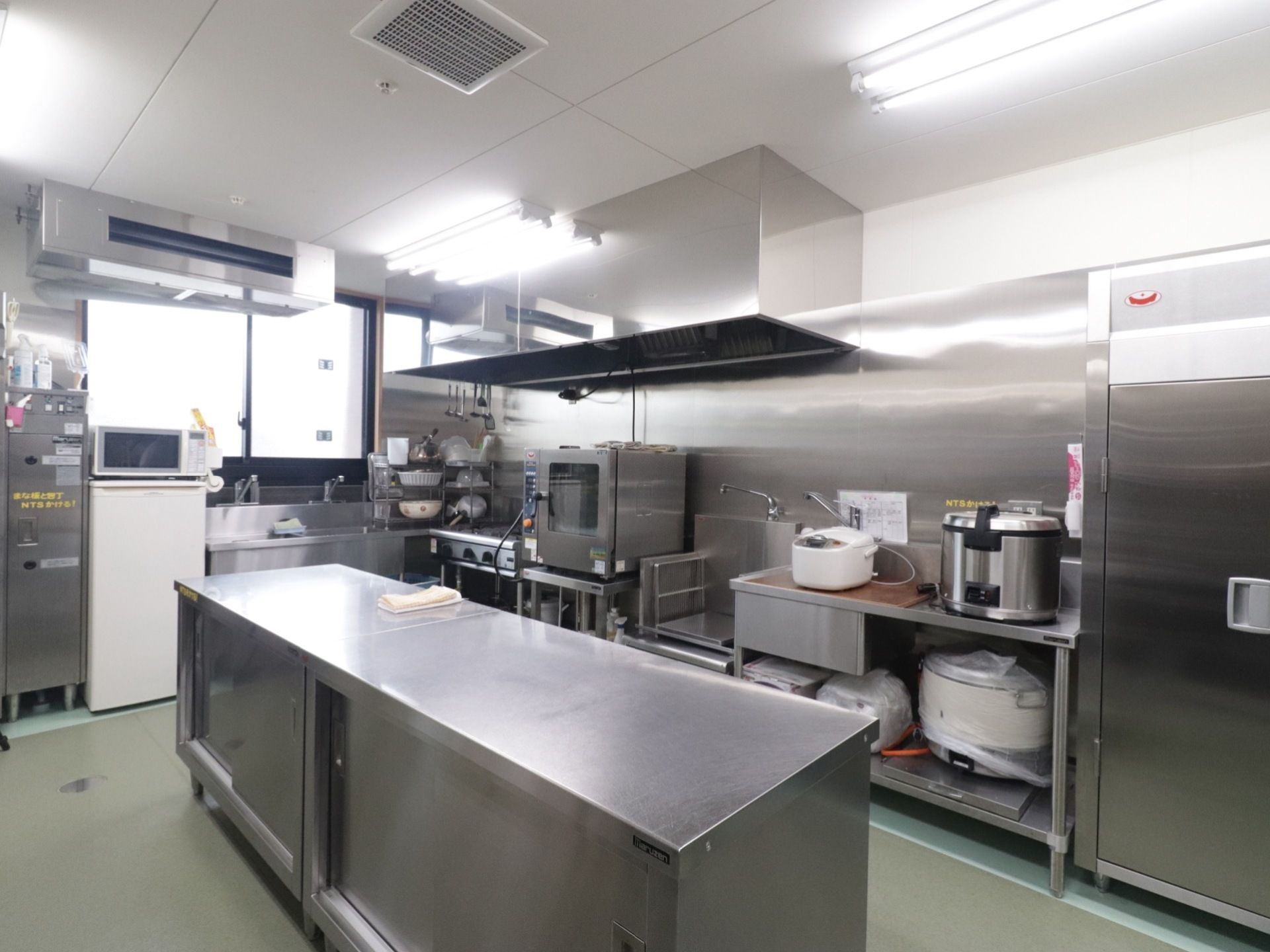 中央にステンレス製の机が設置してある。壁際には炊飯器やコンロなどのたくさんの調理器具が並べて置いてある。