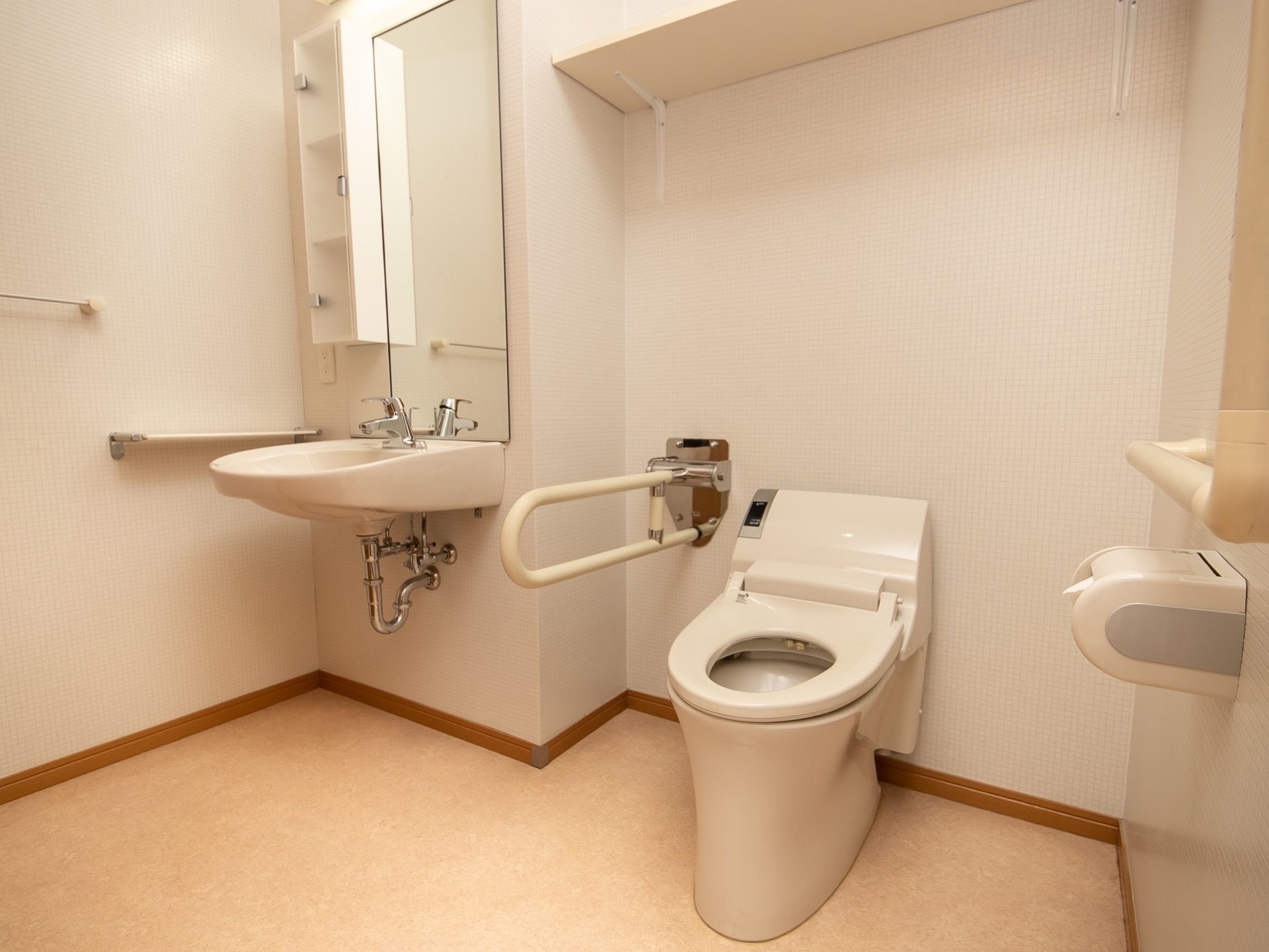可動式の手すりが設置されたトイレである。すぐ側には洗面台があり、鏡や照明や小物の整理棚が備わっている。