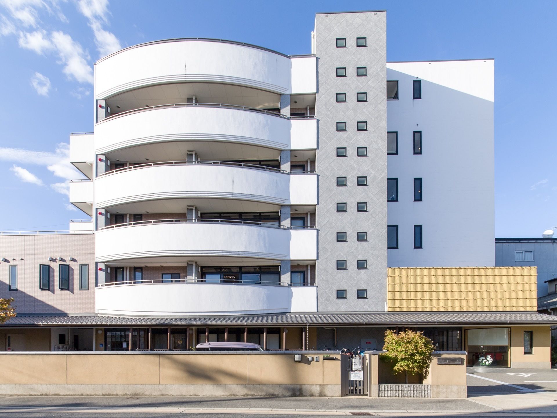 白基調の、現代的な外観をもつ建物である。敷地内には自動車と自転車が停められている。建物内に白い花が飾られているのが見える。