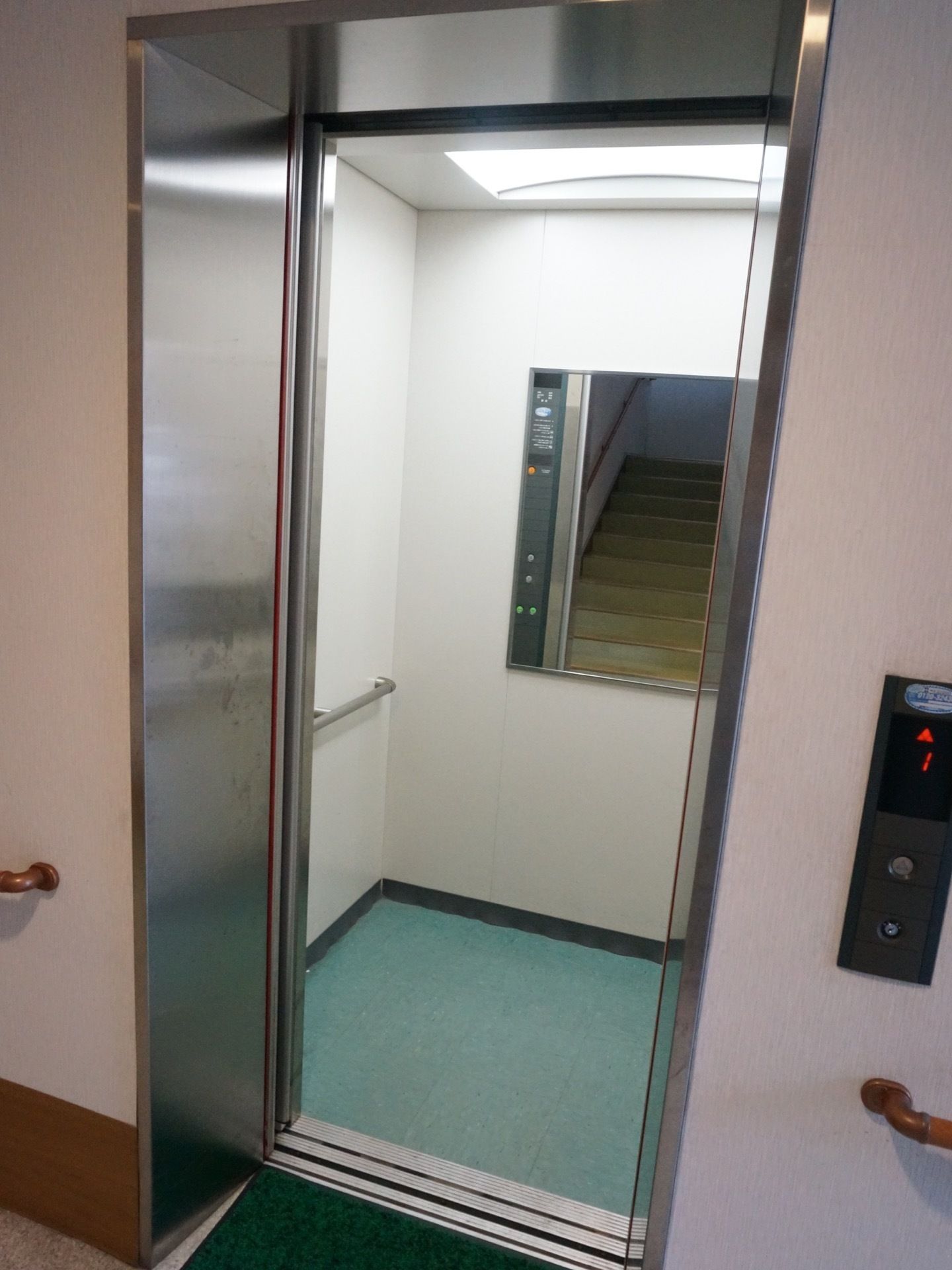 館内には、エレベーターが設置されている。内部には、手すりや鏡が取り付けられている。扉の前には、緑色のマットが敷かれている。