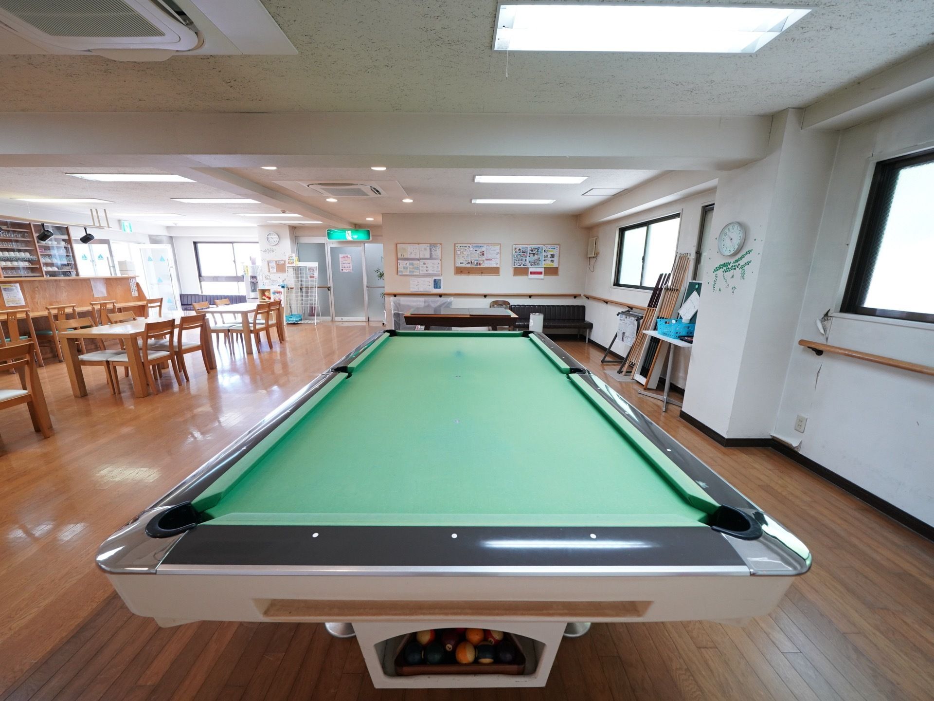 食堂のコーナー部、照明やエアコンの下に、大きなビリヤード台がある。キューも多く備えつけられている。入居者様同士で自由に使用できる。