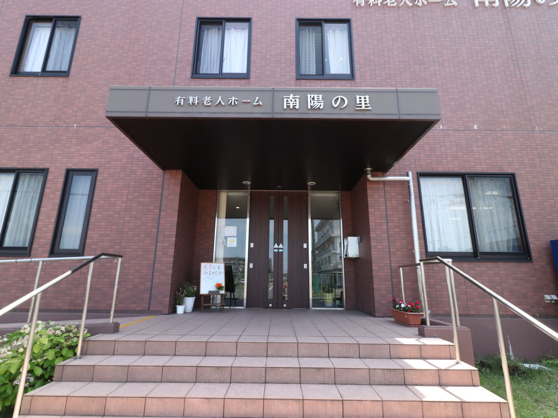 レンガ調のタイル張りの建物で、玄関にはホーム名が付けられている。階段には手すりが付いており、奥にはスロープも設置されている。