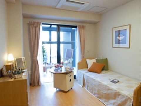 右にベッドとサイドテーブル、左にチェストが置かれた淡い色を基調とした部屋
