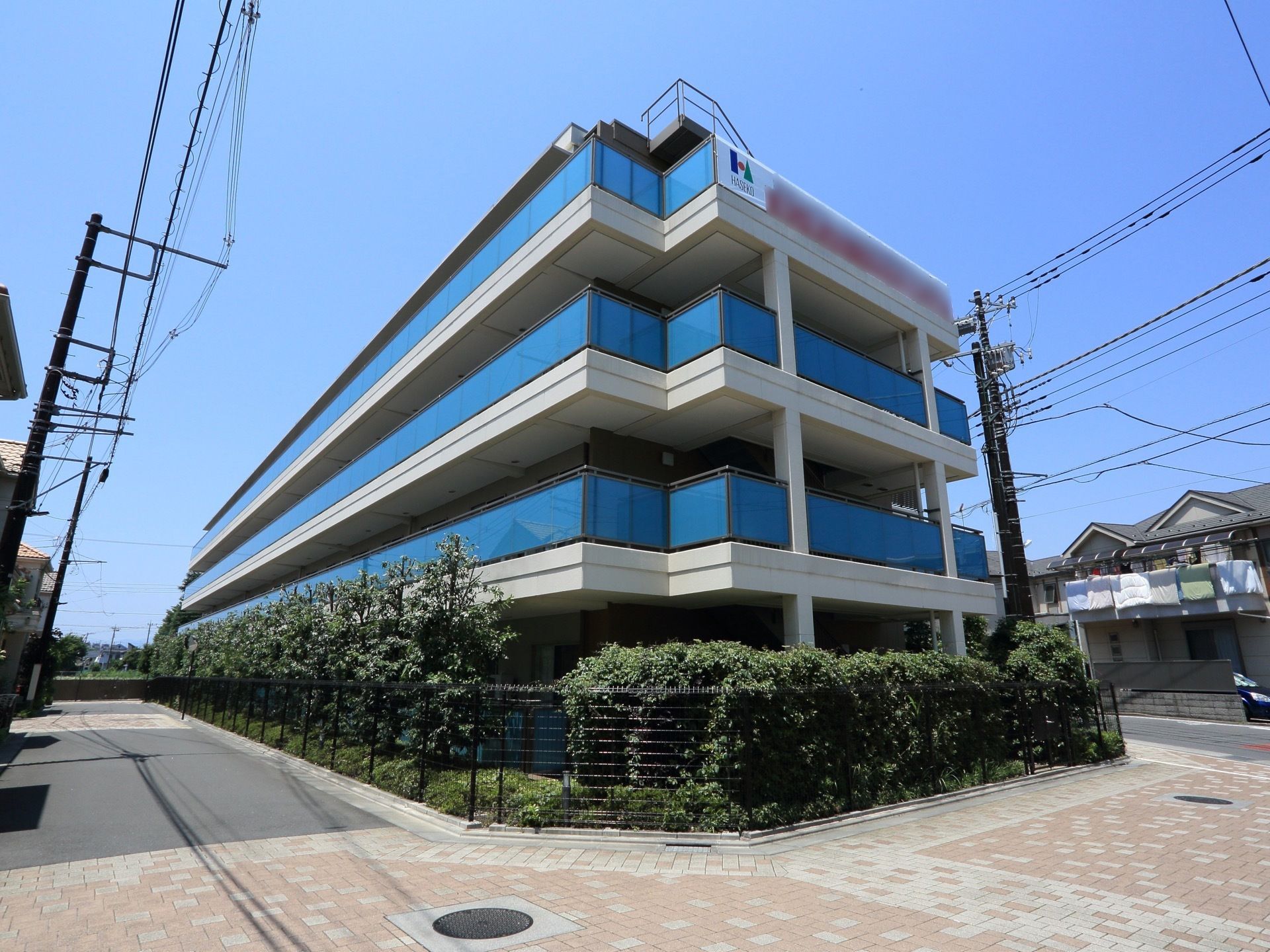閑静な住宅街に佇む４階建ての建物である。敷地の境界に黒格子のフェンスを設け、周りにはたくさんの樹木を植え付けている。