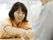 オレンジ色の半袖の制服を着た女性スタッフが両手で何かを差し出している。テーブルをはさんで入居者様が座っている。
