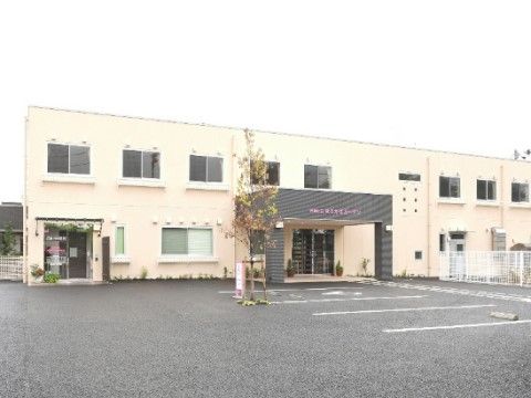 黒い屋根のあるエントランス前に広い駐車場のある、2階建ての建物