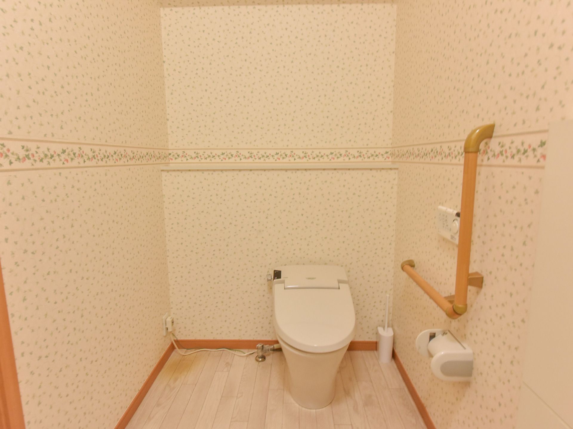 絵柄の付いた壁紙のトイレである。向かって右側には手摺が設置されている。小さなカウンターが壁の中段くらいにある。