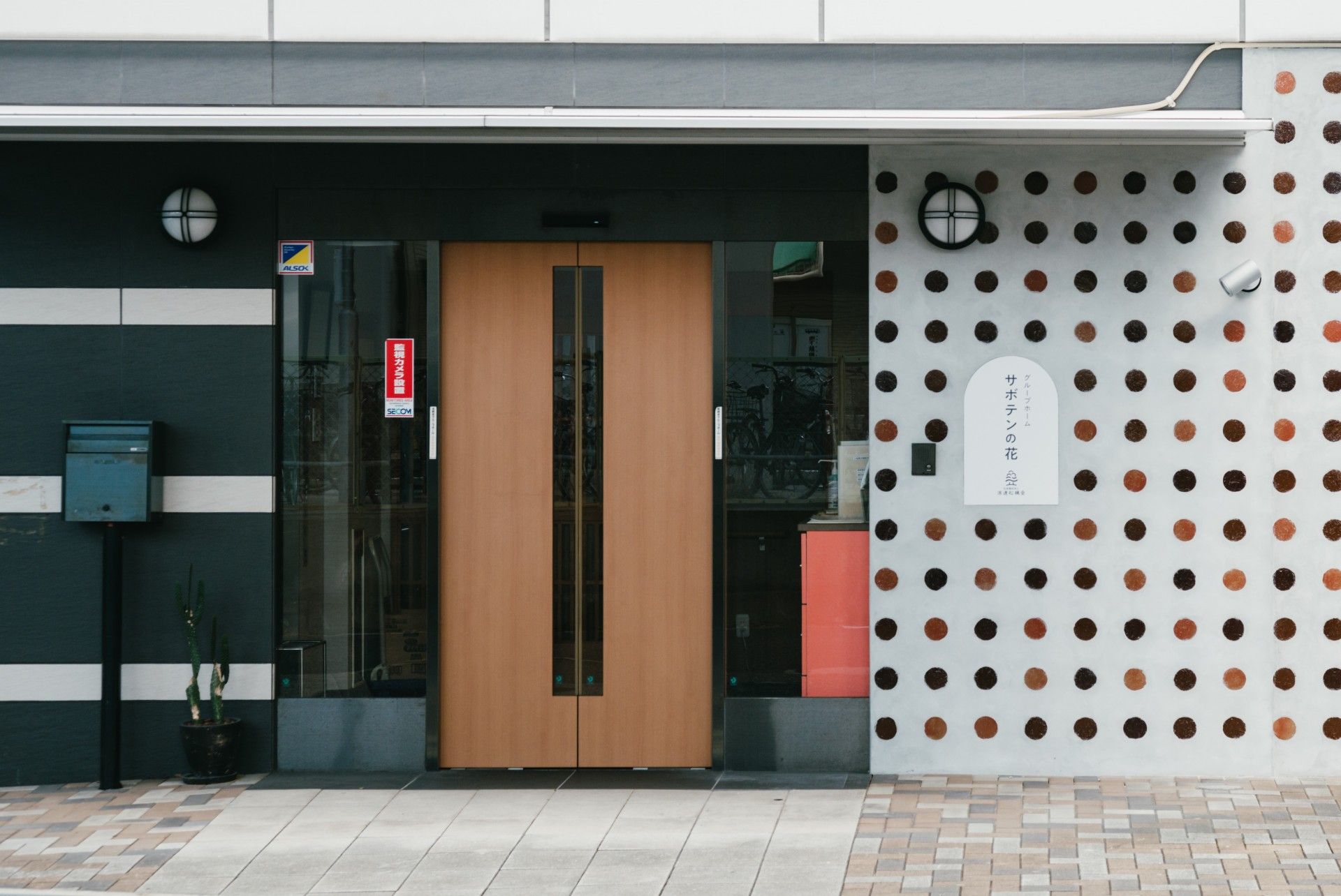 玄関入口には大きな扉が設置されている。扉のガラス部分にはAED装置と防犯カメラ設置を示すステッカーが貼られている。