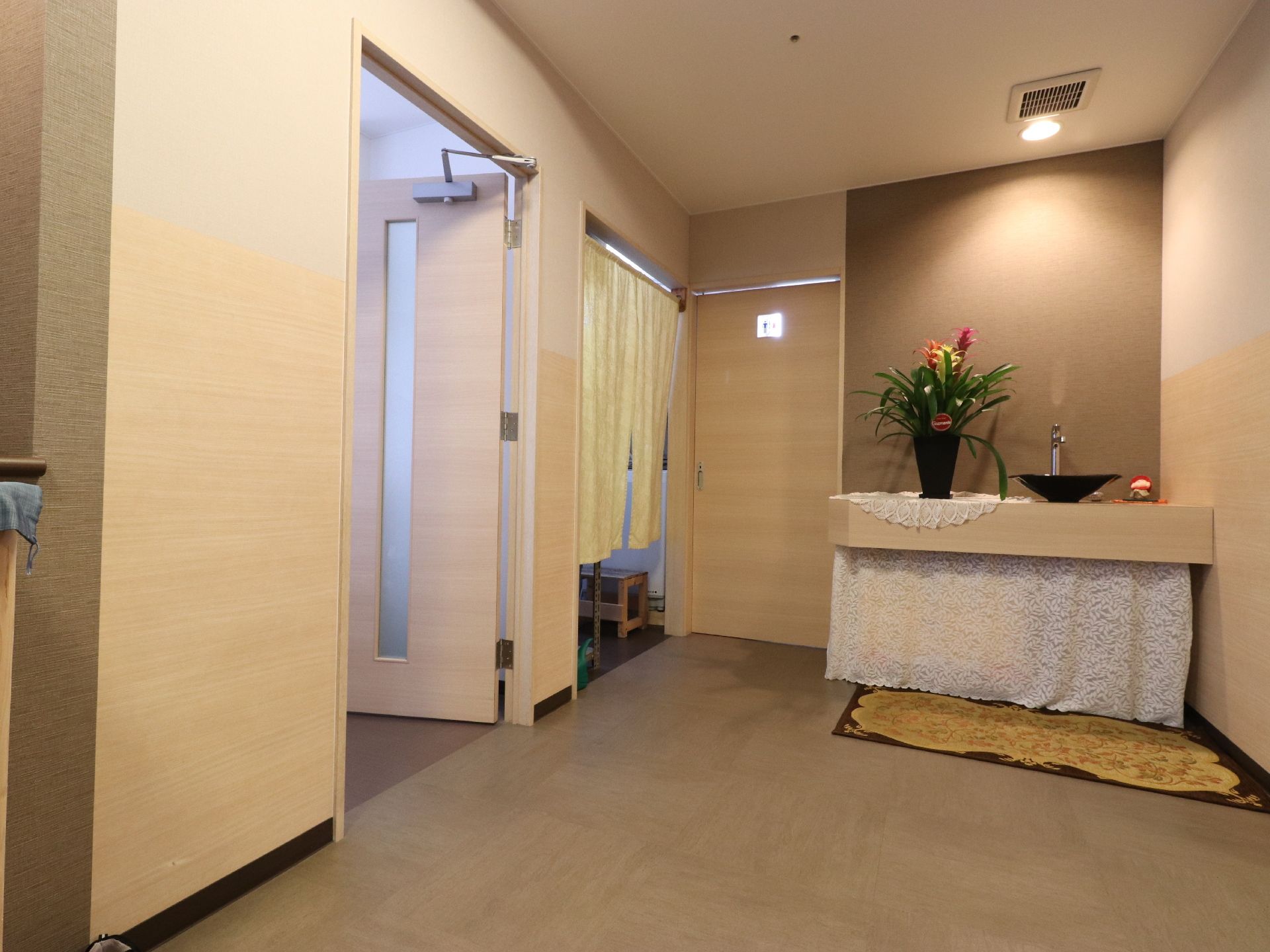 ベージュやブラウンを用いた品の良い和風旅館を連想させる廊下。突き当たりの間接照明の下には華やかな植木鉢が置かれている。