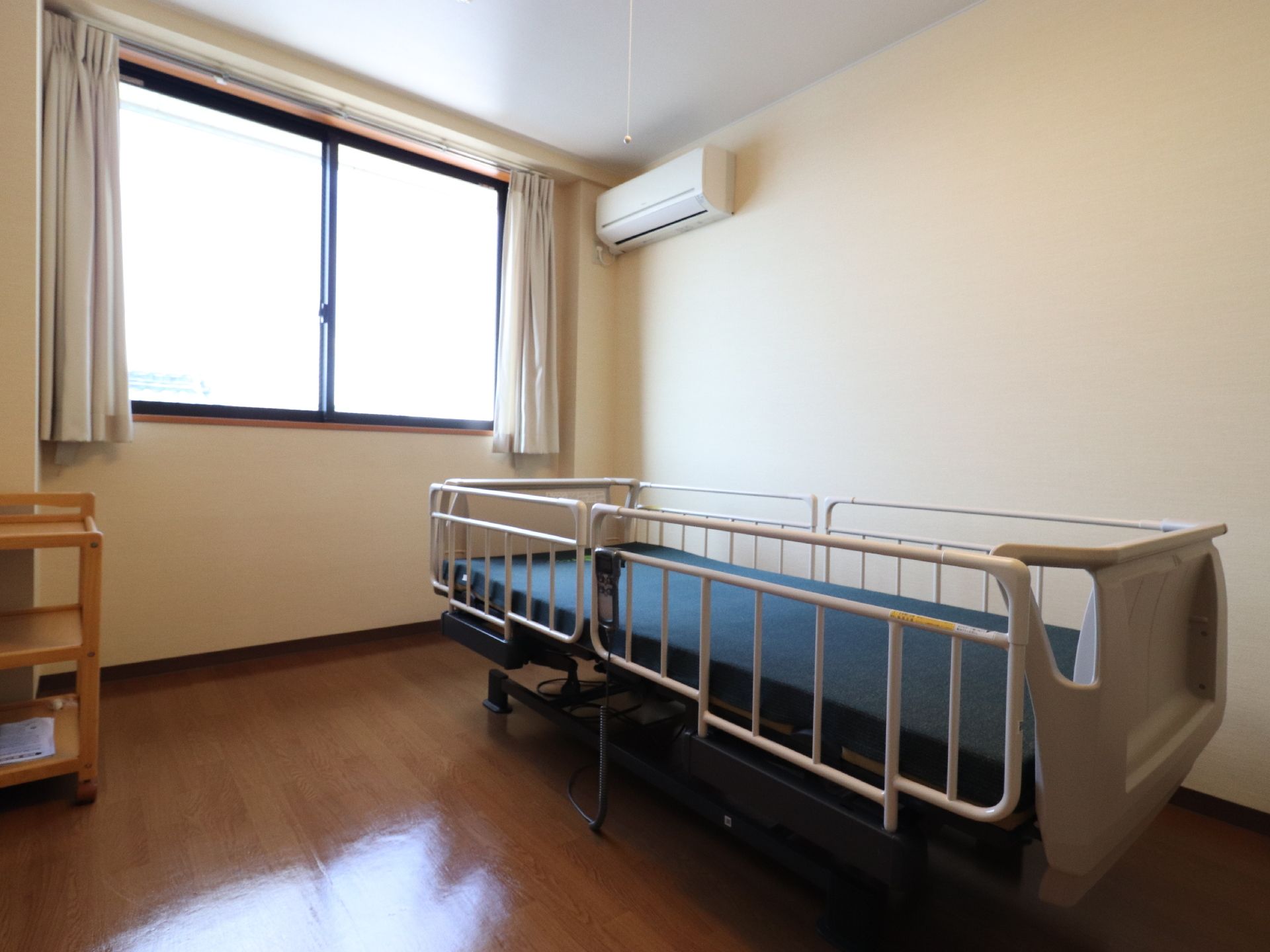 窓のある個室には、介護ベッドやエアコンが置かれている。壁にはエアコンが設置されており空調を調節することができる。
