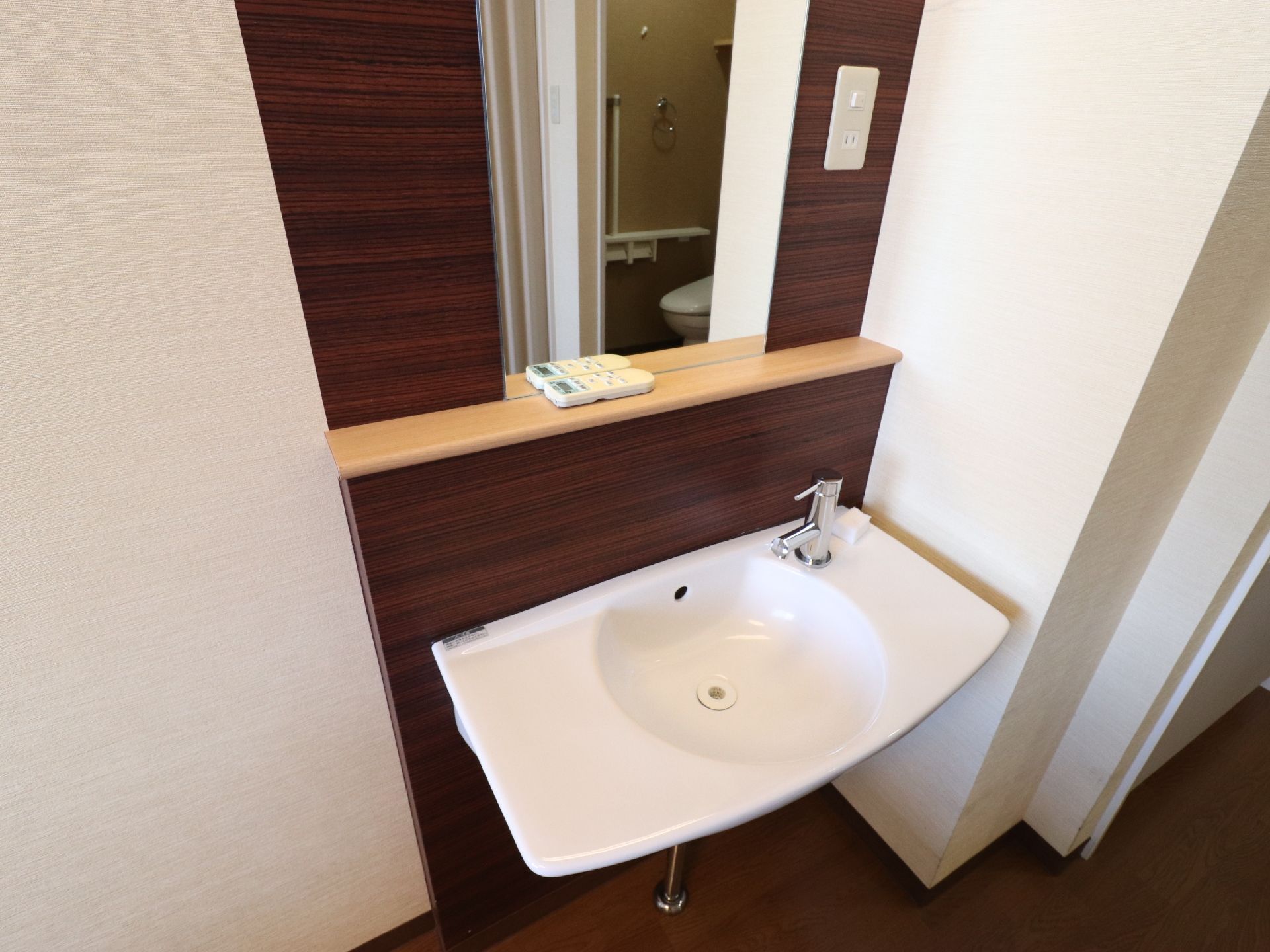 部屋についている洗面台は白でとてもスタイリッシュ。大きな鏡の横には、照明のスイッチとコンセントがある。