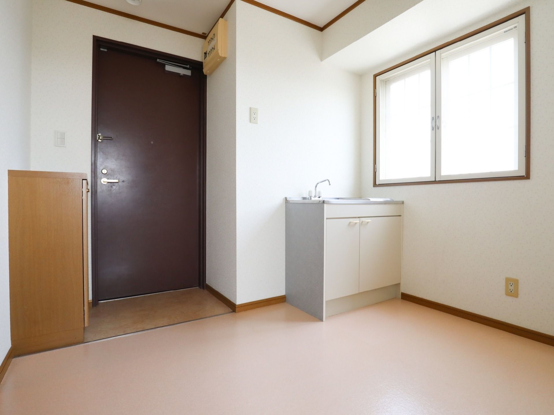 白い壁にドアや窓枠の茶色がアクセントの居室には、窓があり、靴箱、ミニキッチンが備えられている。また、入り口には段差がない。