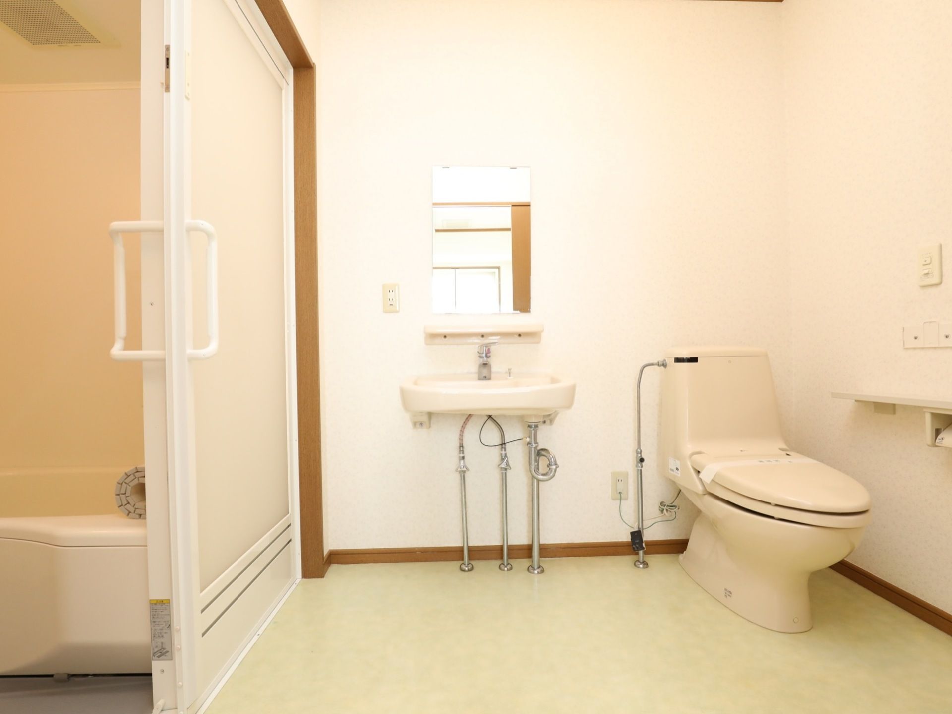 アイボリーで落ち着いた色調のトイレと浴室は引き戸で仕切られている。トイレには洗面も鏡もあり、手すりも備えている。