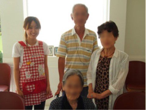 茶色の椅子が置かれた施設内の室内に並ぶ入居者3人と笑顔の職員