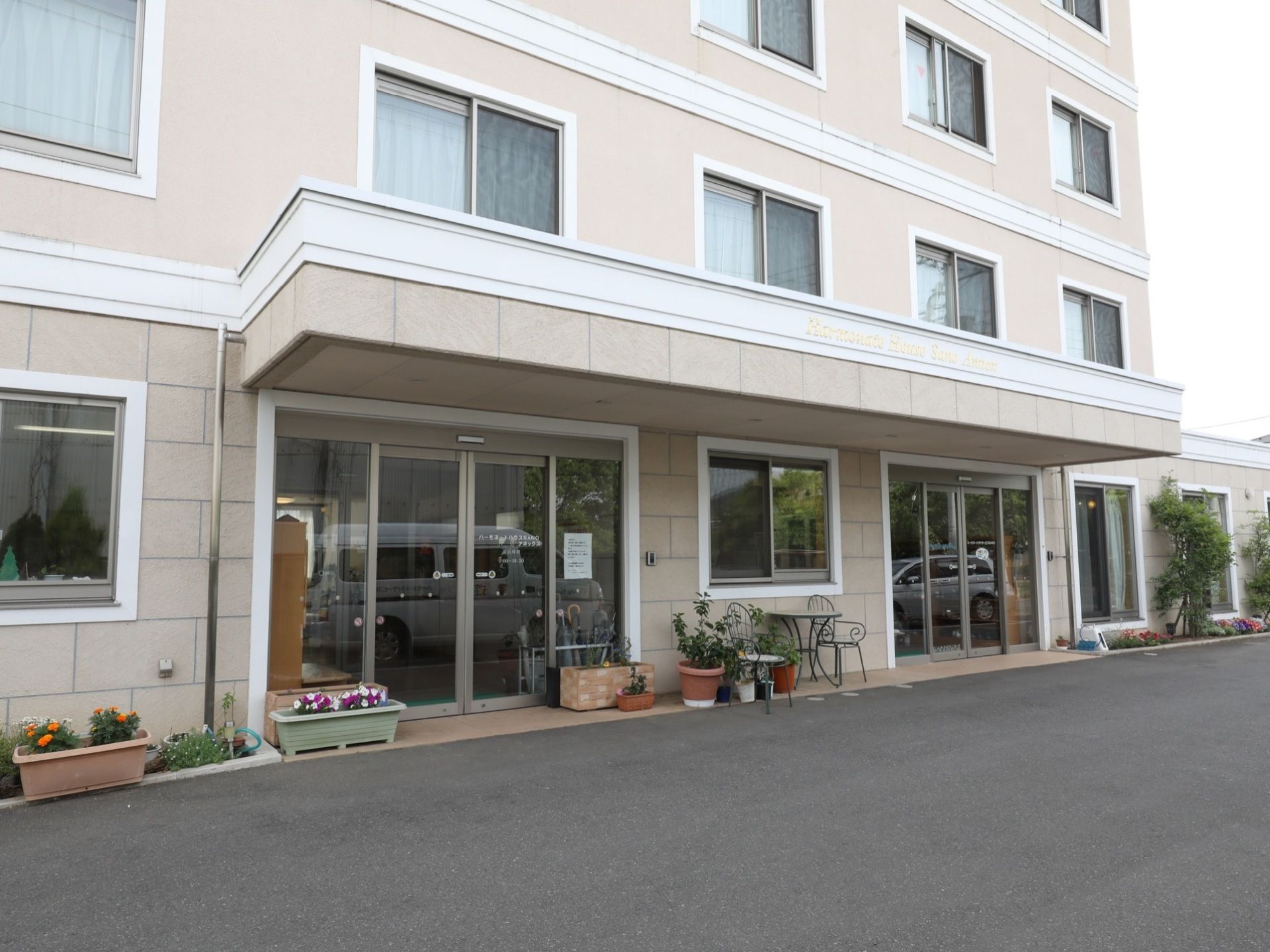 施設建物の正面玄関の外観。二つ設けられている自動ドアの中央には、プランターに混じってエクステリアも兼ねた座席が置いてある。