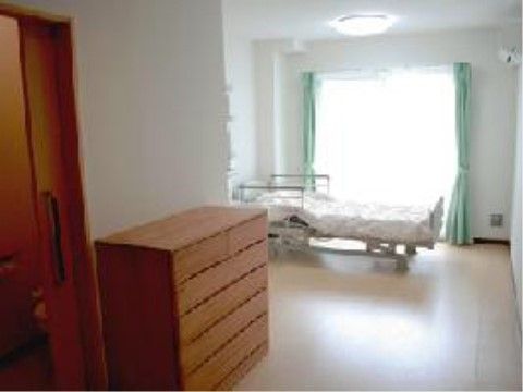 室内の窓際に置かれた介護ベッドとブラウンのチェスト
