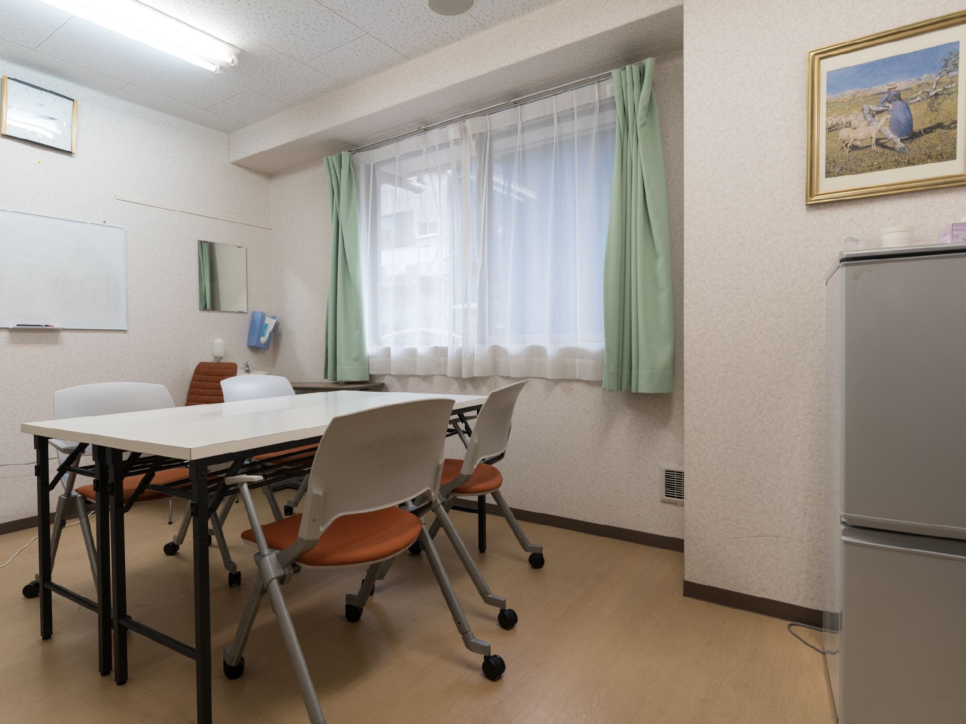 洗面台があり、液体ソープ入れが取り付けてある。窓には緑色のカーテンが設置済み。白いテーブルと椅子が並べてある。