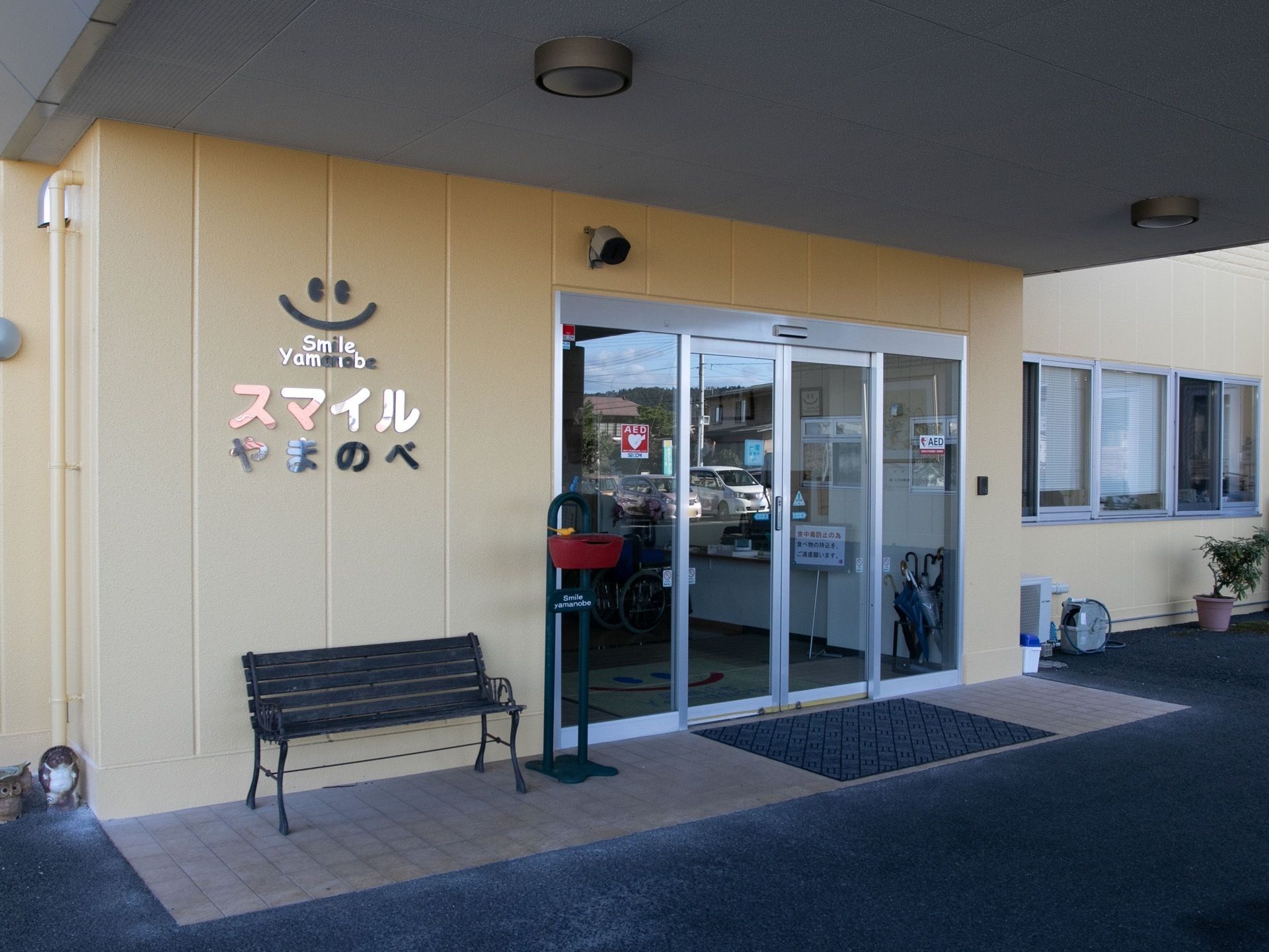 クリーム色の外壁に鏡面仕上げの施設ロゴが貼られている。屋根は大きく、段差のないフラットな玄関入口である。