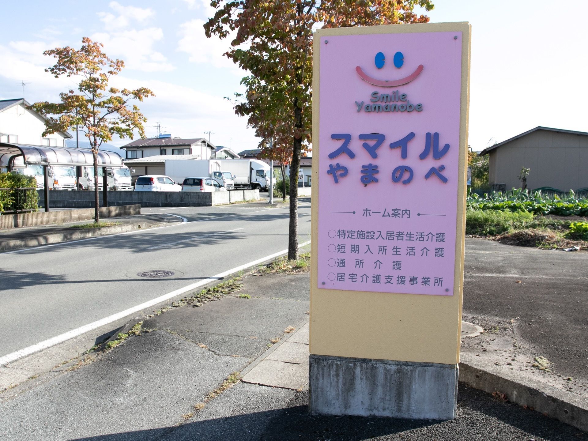 クリーム色の門柱に、施設名と施設の案内を載せたピンクの看板が設置されている。車で走っていても見やすい位置に置かれている。