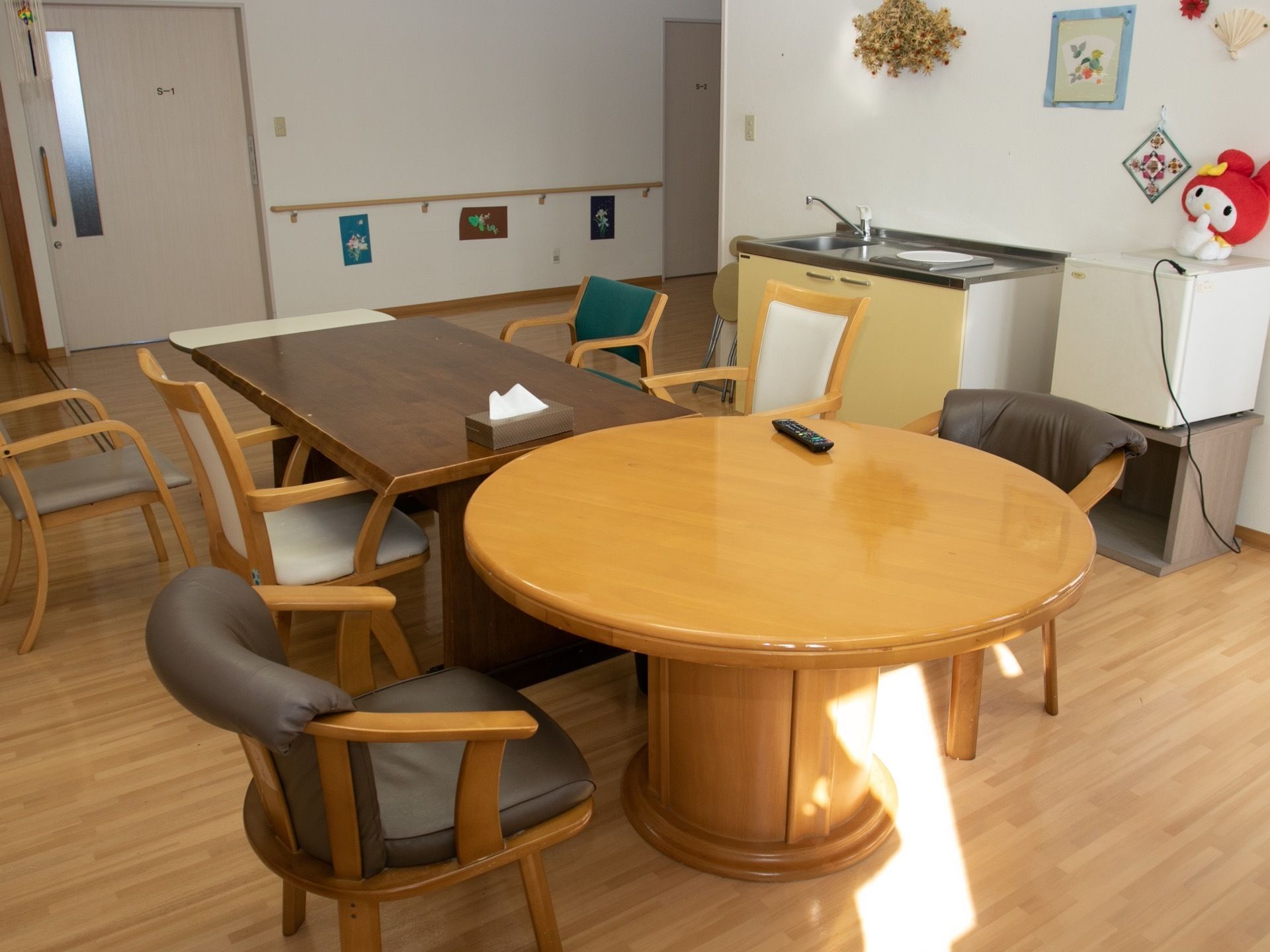 丸いテーブルと長テーブルが並べられ、椅子が置かれた共有スペースである。簡単なキッチン設備と冷蔵庫が設置されている。