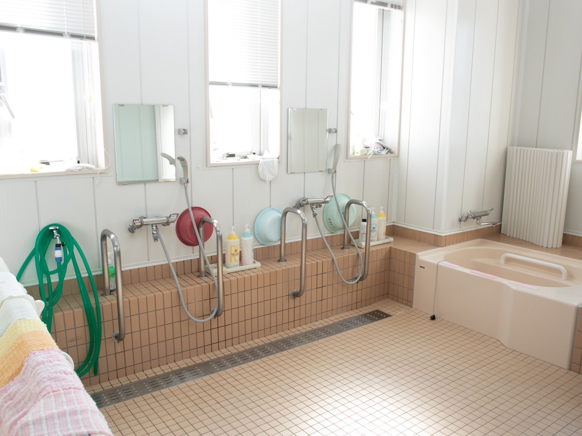 ピンク色のタイル張りの浴室である。シャワー設備が設けられ、鏡や手すりがある。個浴のできる小さなバスタブもある。