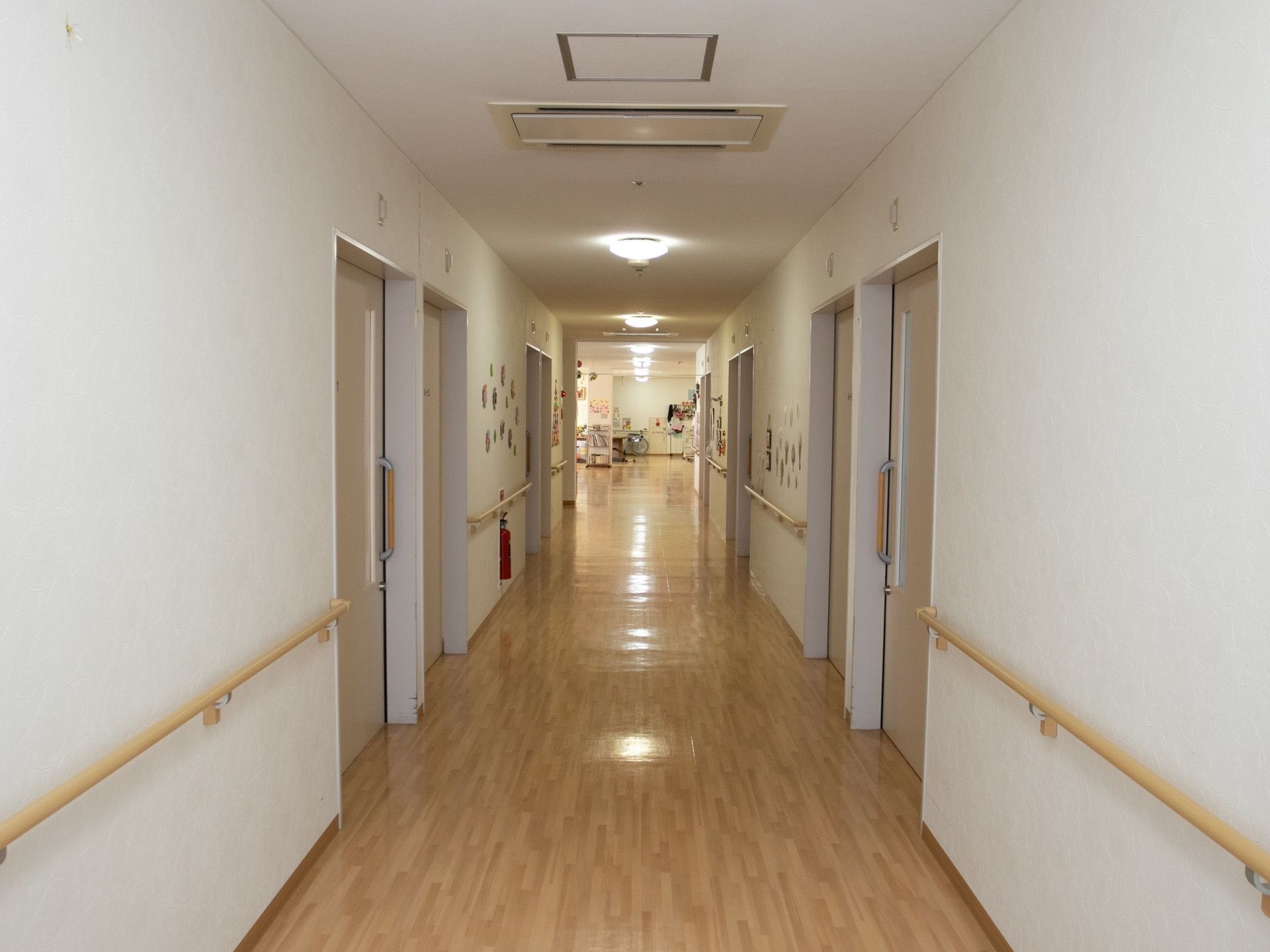 淡い色のフローリングで明るい雰囲気の廊下である。壁に設置された手すりや引き戸も木目調で統一感がある。