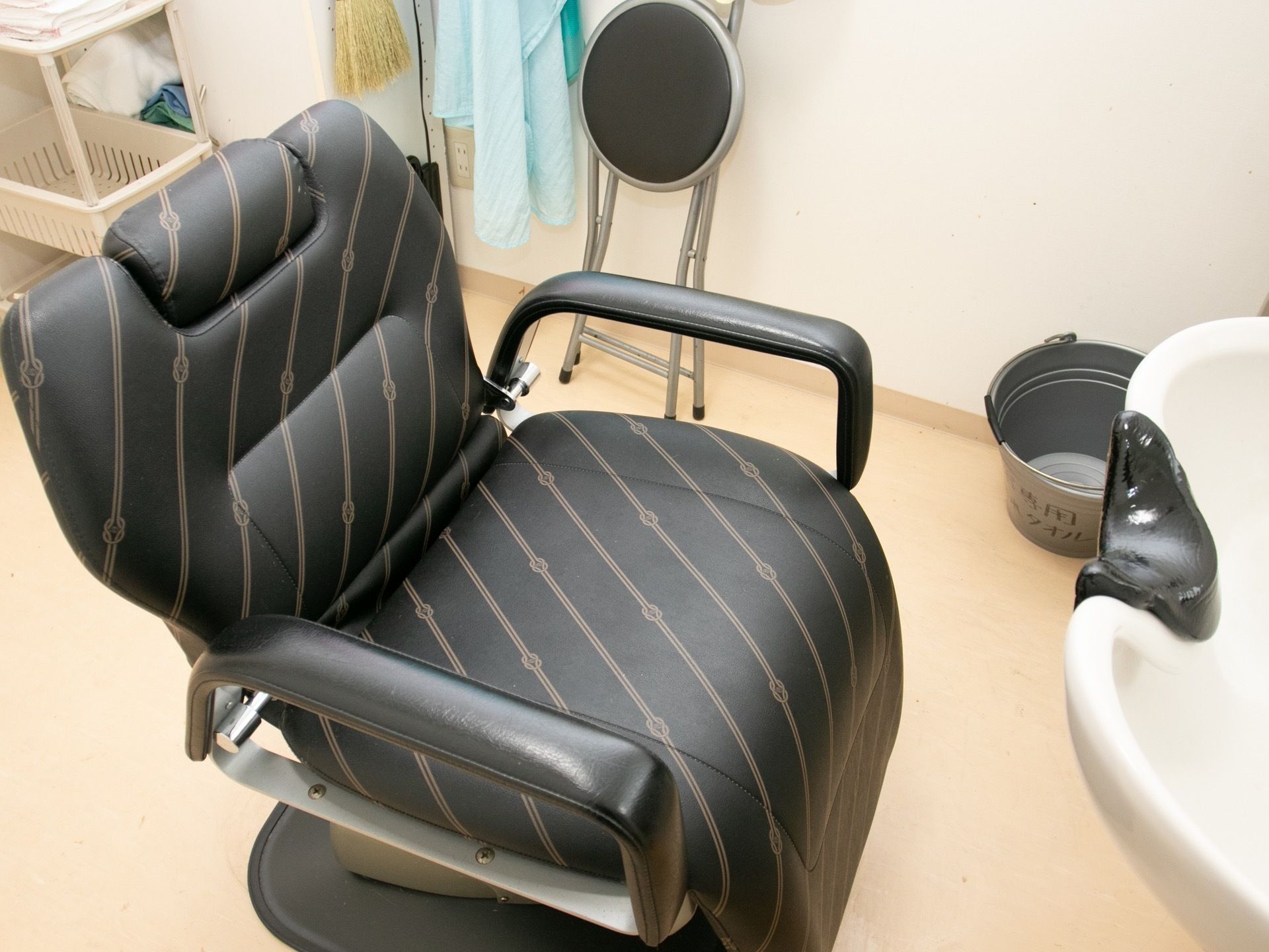理容室に用意されている洗髪台と椅子である。黒に茶色のラインが斜めに入った革製の椅子で、肘置きがついている。