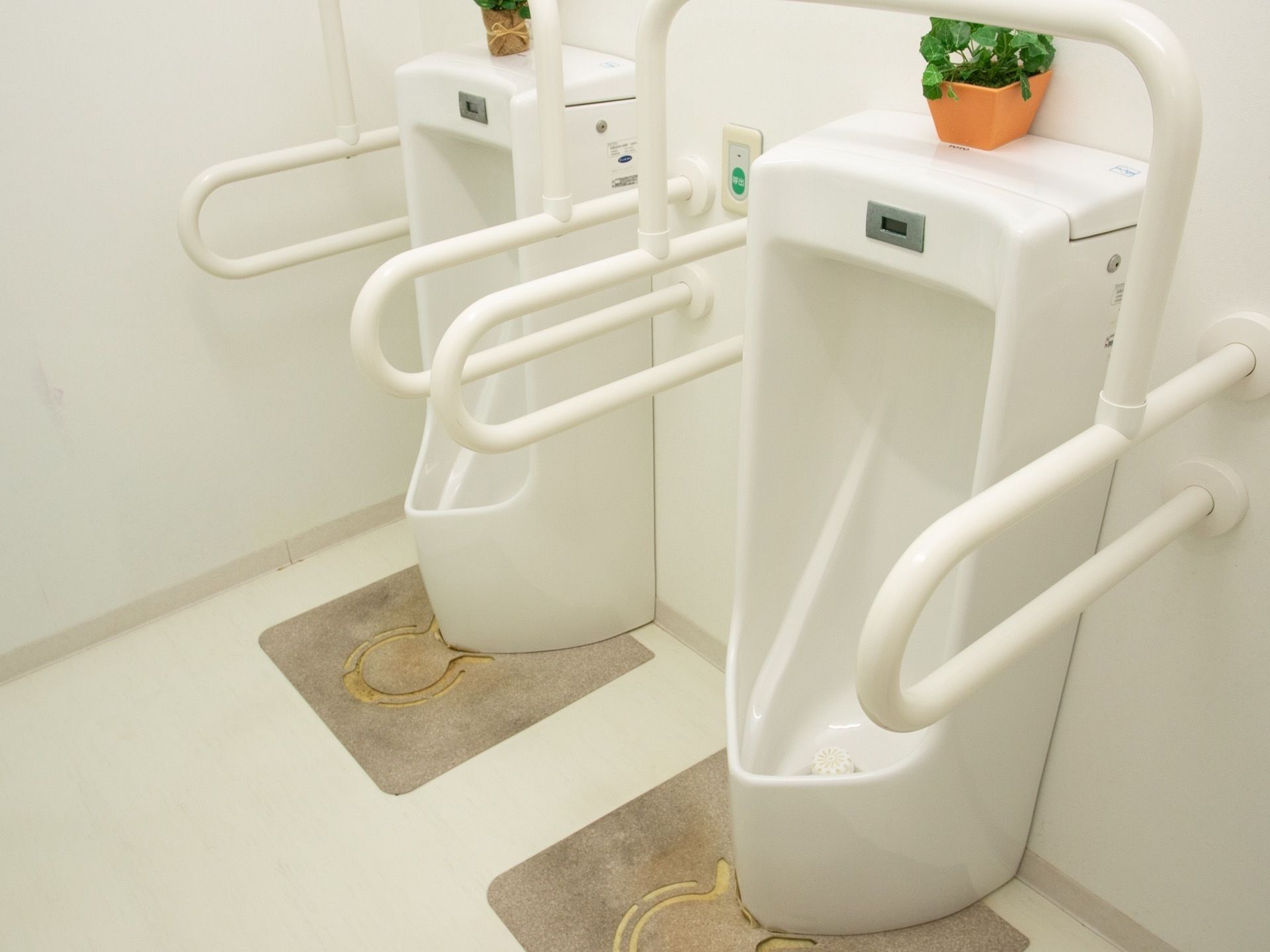 男性の小便用の便器が２台設置されている。センサー式で、手すりが取り付けられている。便器の上にはグリーンが置かれている。