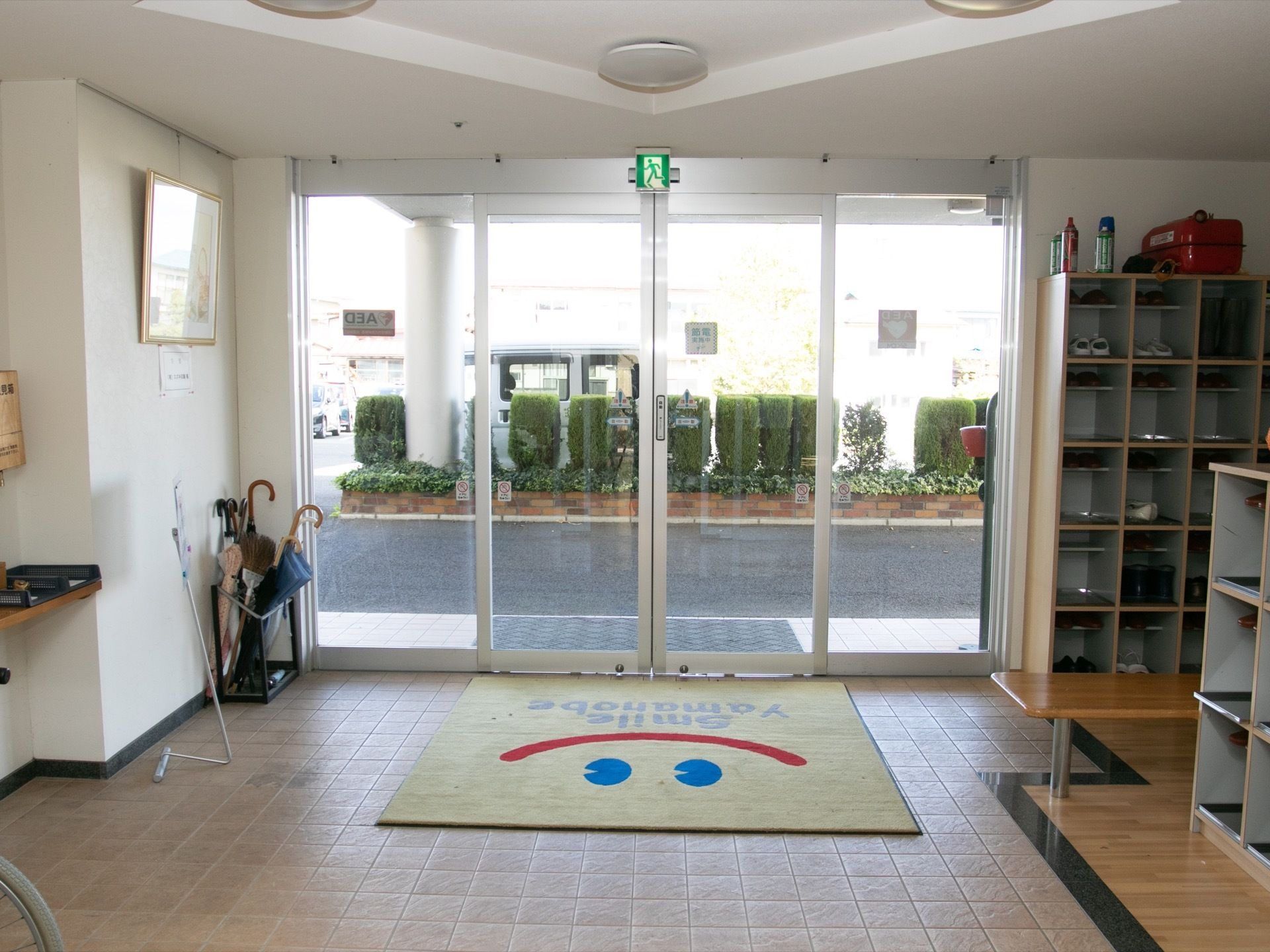 オートドアの玄関である。床にはマットが敷かれ、下駄箱が設置されている。天井には照明や誘導灯が取り付けられている。