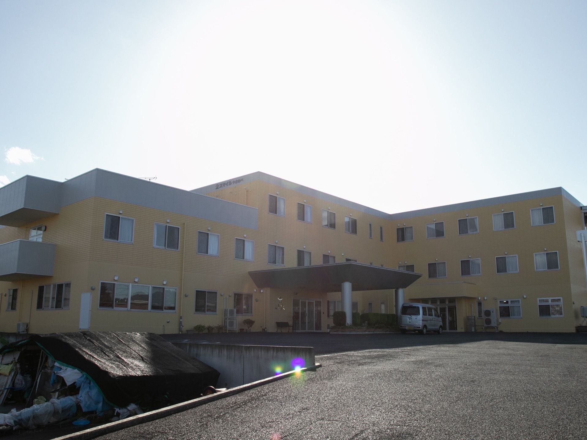 クリーム色とグレーの外壁が特徴的な３階建ての施設建物である。玄関の屋根が大きく、丈夫でしっかりとした印象である。