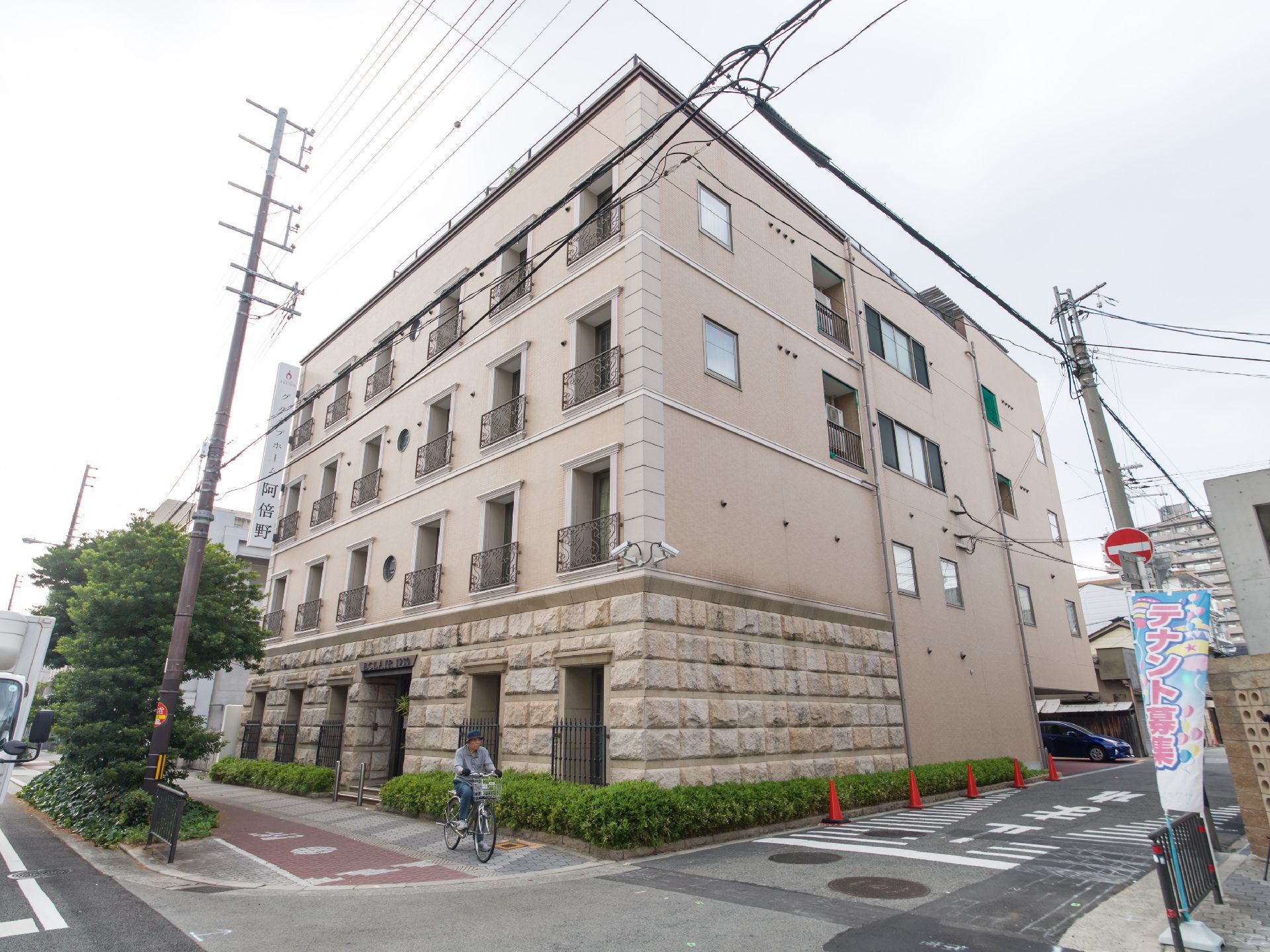 施設の建物はベージュ色で、1階の前面と横には凹凸が付けられている。前面は歩道で、境には植え込みが設けられている。