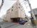 施設は4階建ての建物である。外壁は明るいベージュ色で、各面に四角い窓が設けられている。駐車スペースの地面は茶色に塗られている。