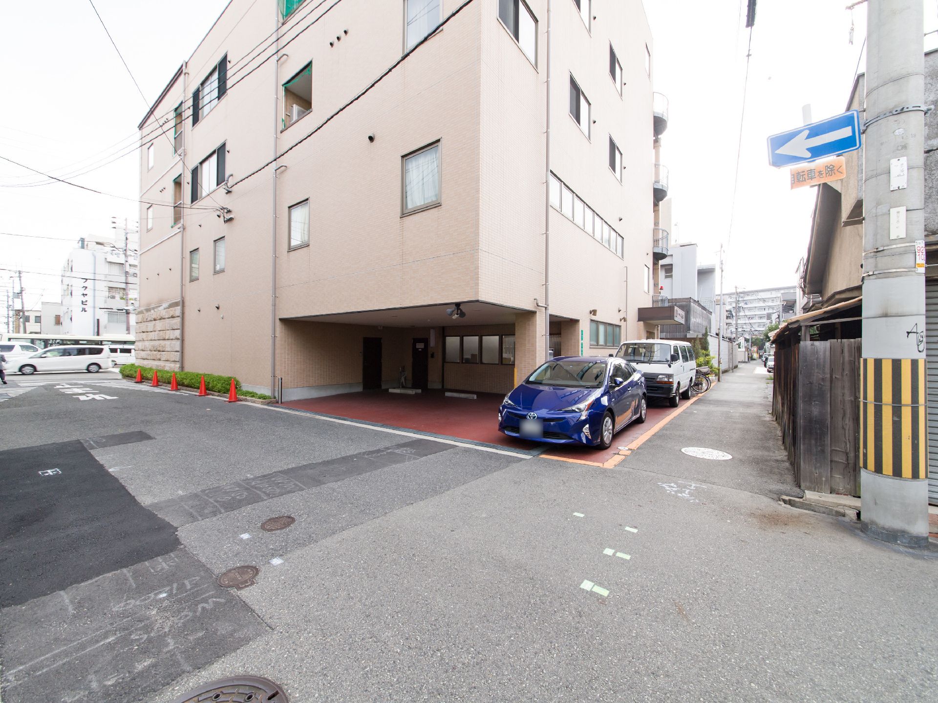 施設の建物は4階建てである。1階の角部分には空間が設けられ、駐車スペースとなっている。建物の右側に車と自転車が停められている。