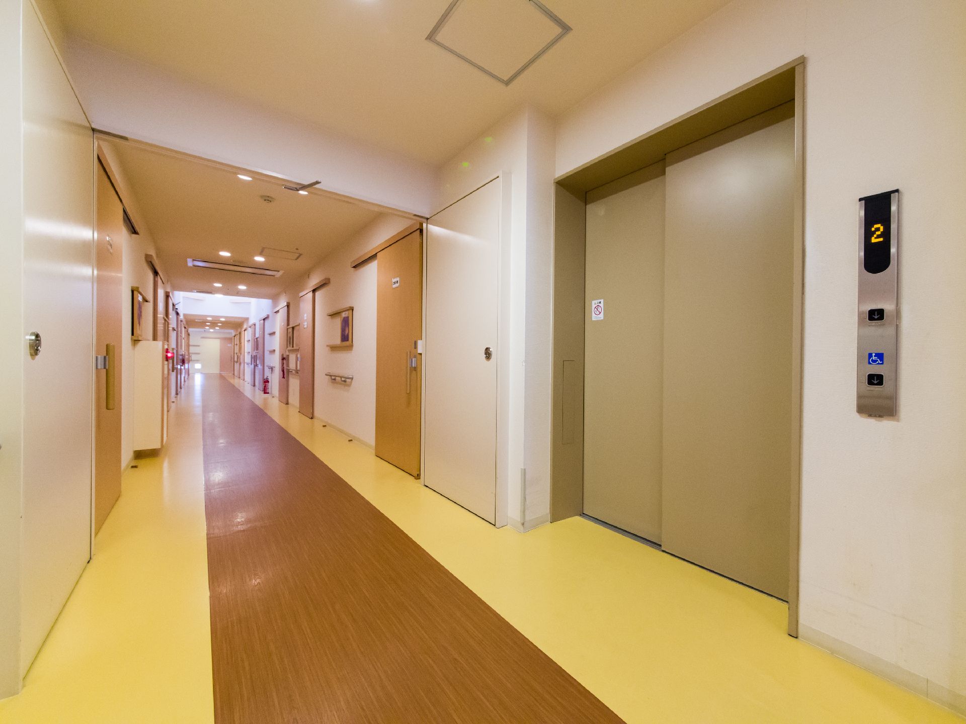右手前にはエレベーターが1基ある。床はクリーム色と茶色の2色から構成されている。廊下の左右にはいくつかの扉が並んでいる。