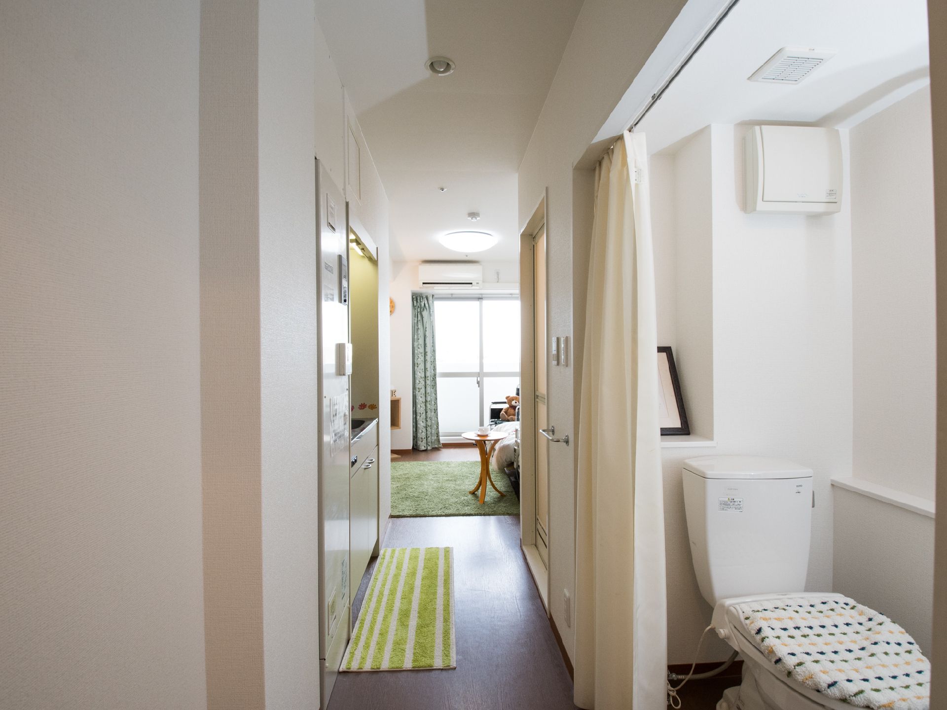 白を基調とした居室。小さなキッチンやエアコンが設置されており、トイレの入口はドアではなくカーテンになっている。