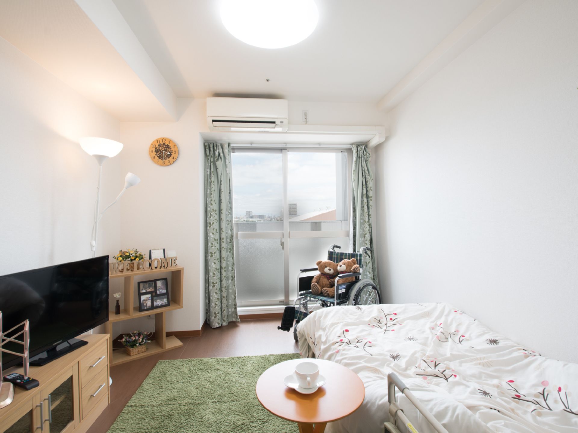 白い壁紙の居室。床にはグリーンのカーペットが敷かれている。大きなテレビが設置され、窓からは景色が見える。