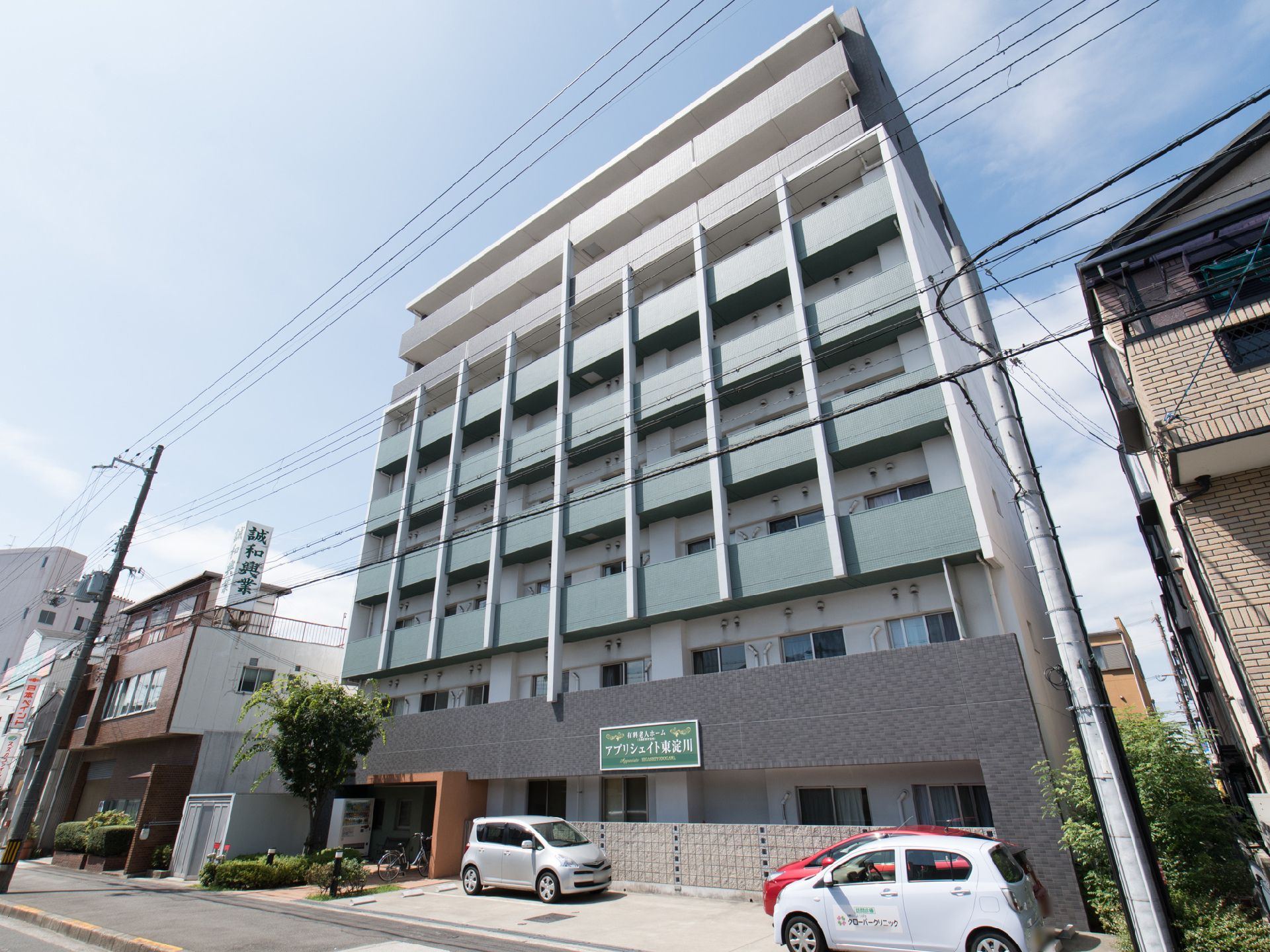 9階建ての建物で、施設前には駐車場がある。玄関前に飲み物の自動販売機が設置してある。木が植えられている。