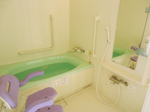 手すりが配置された安心して入浴できる浴室。鏡のそばに棚があるので入浴用品を置くことができる。介護用シャワー椅子も設置。