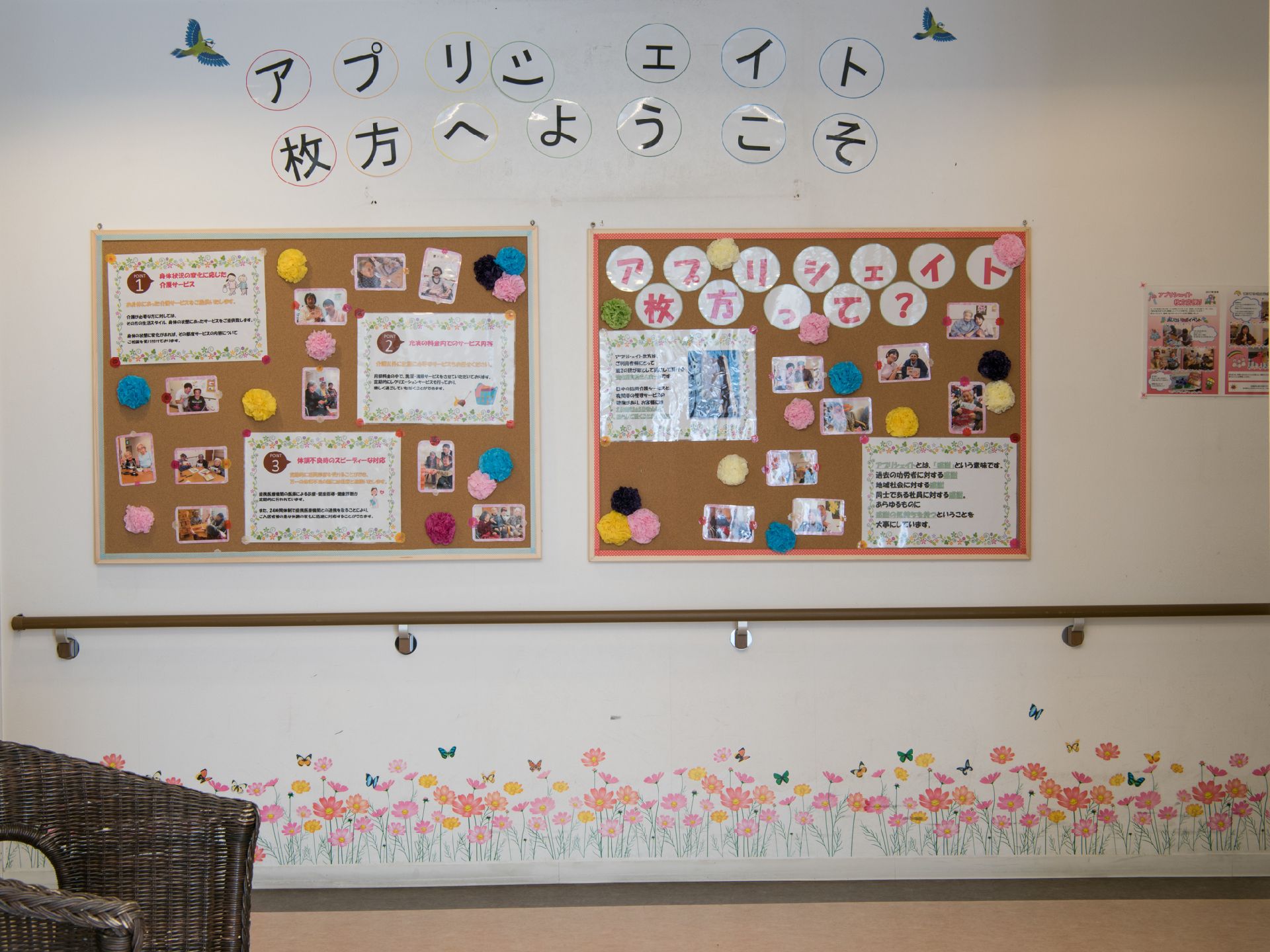 廊下の壁に「ようこそ」の文字が貼られている。その下には、写真や施設についての説明が書かれた紙が、コルクボードに貼られ掲示されている。